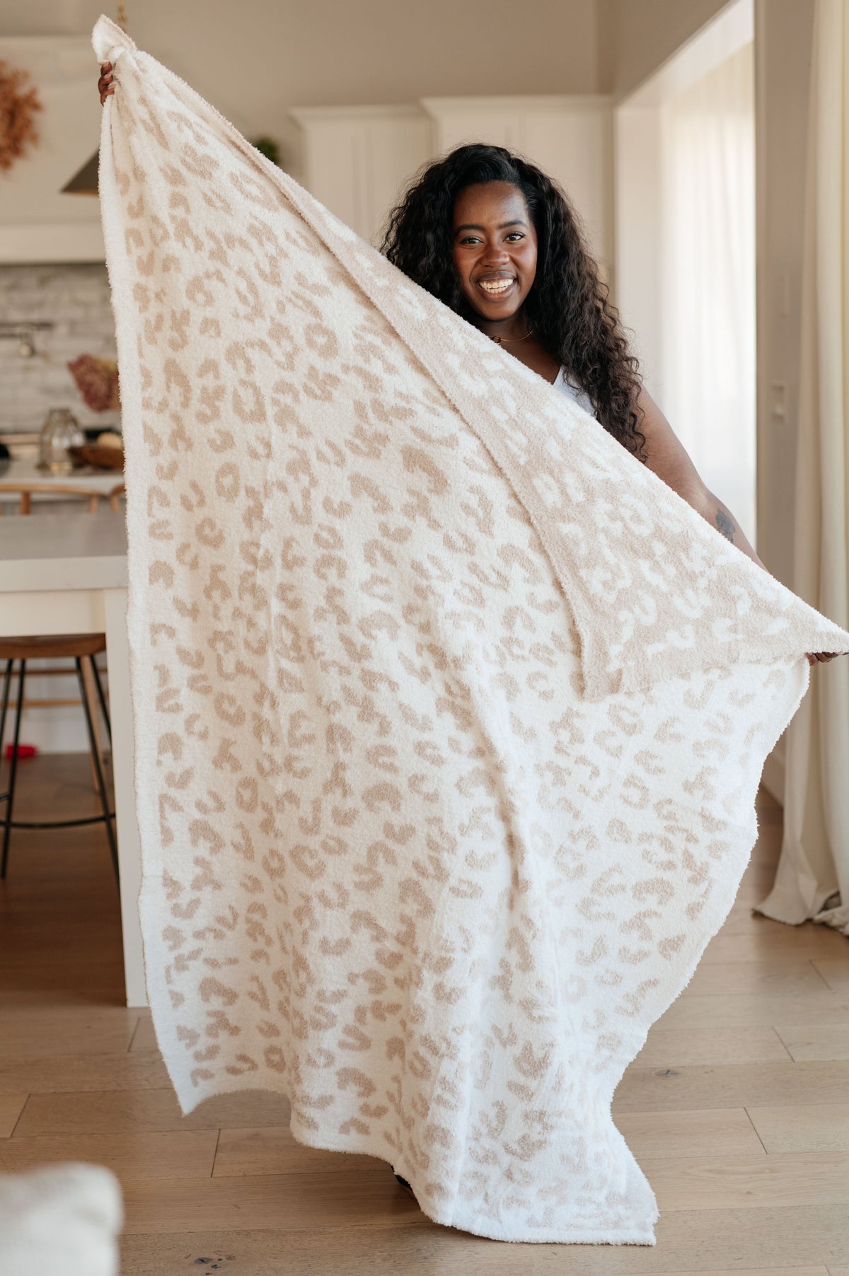 A plush blanket with a neutral animal pattern held by a smiling person in a cozy room.