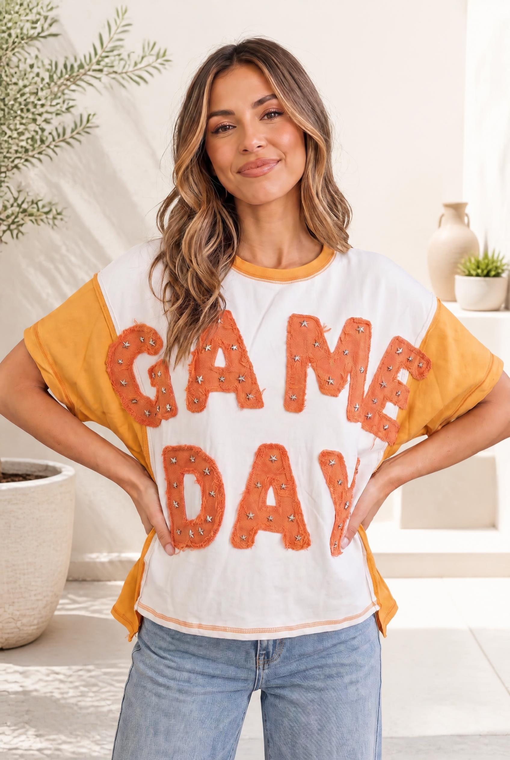 A woman wearing an oversized cream tee with mustard sleeves, featuring orange chenille letter patches with star studs.