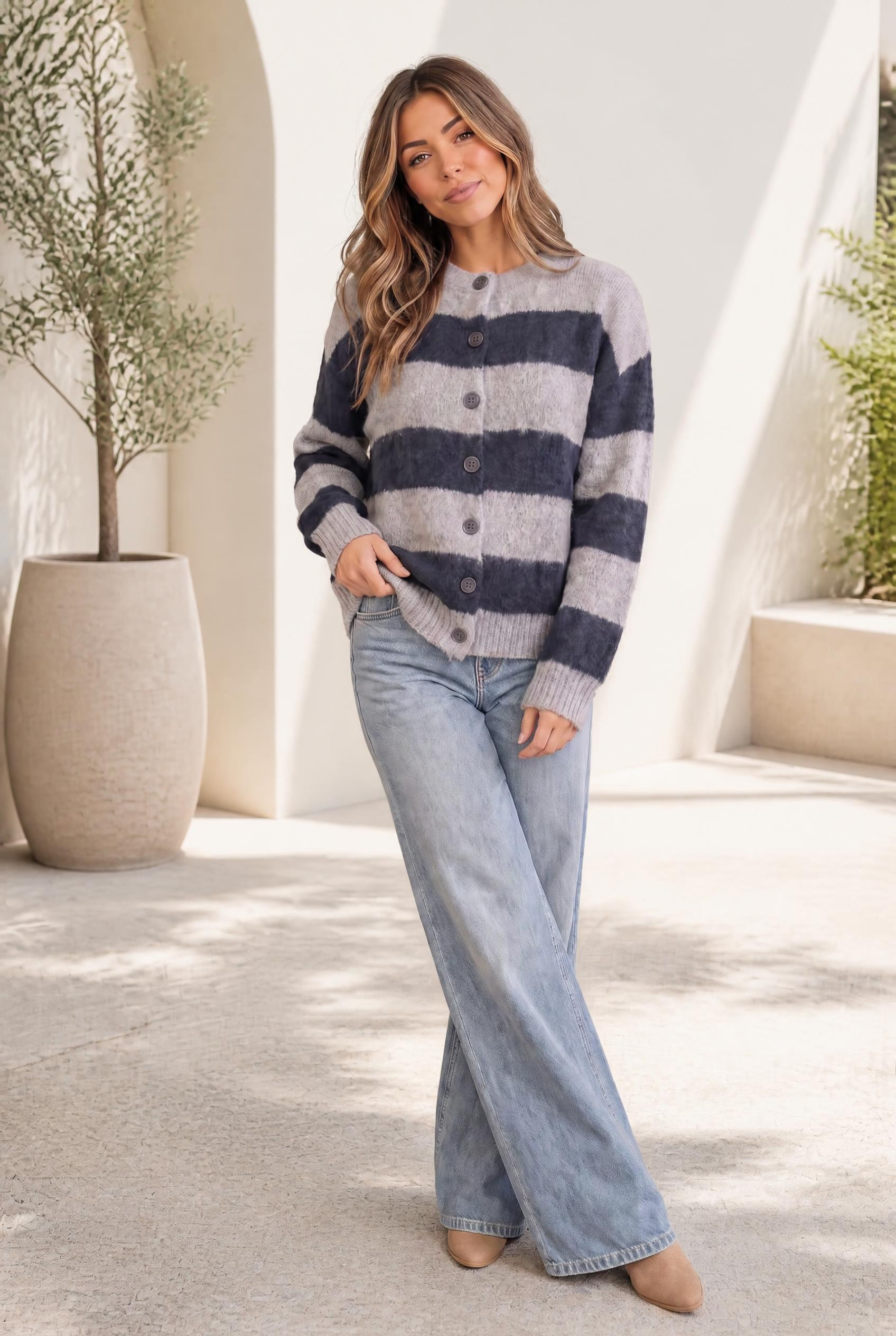A woman wearing a fuzzy oversized cardigan with navy and grey wide stripes, buttoned front, and ribbed cuffs and hem.