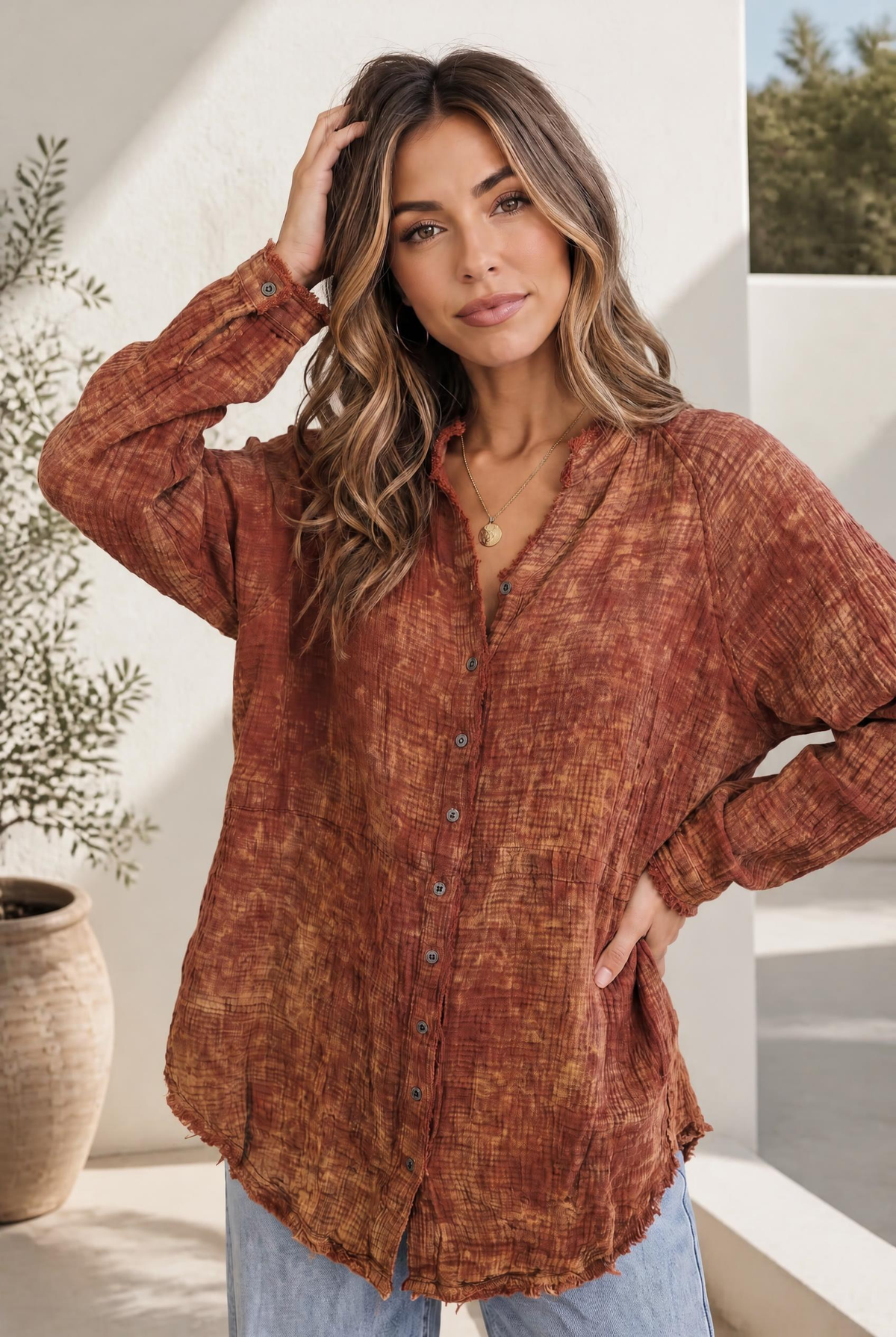 Woman wearing a rust and gold washed button-down gauze shirt with an oversized fit and frayed hem.