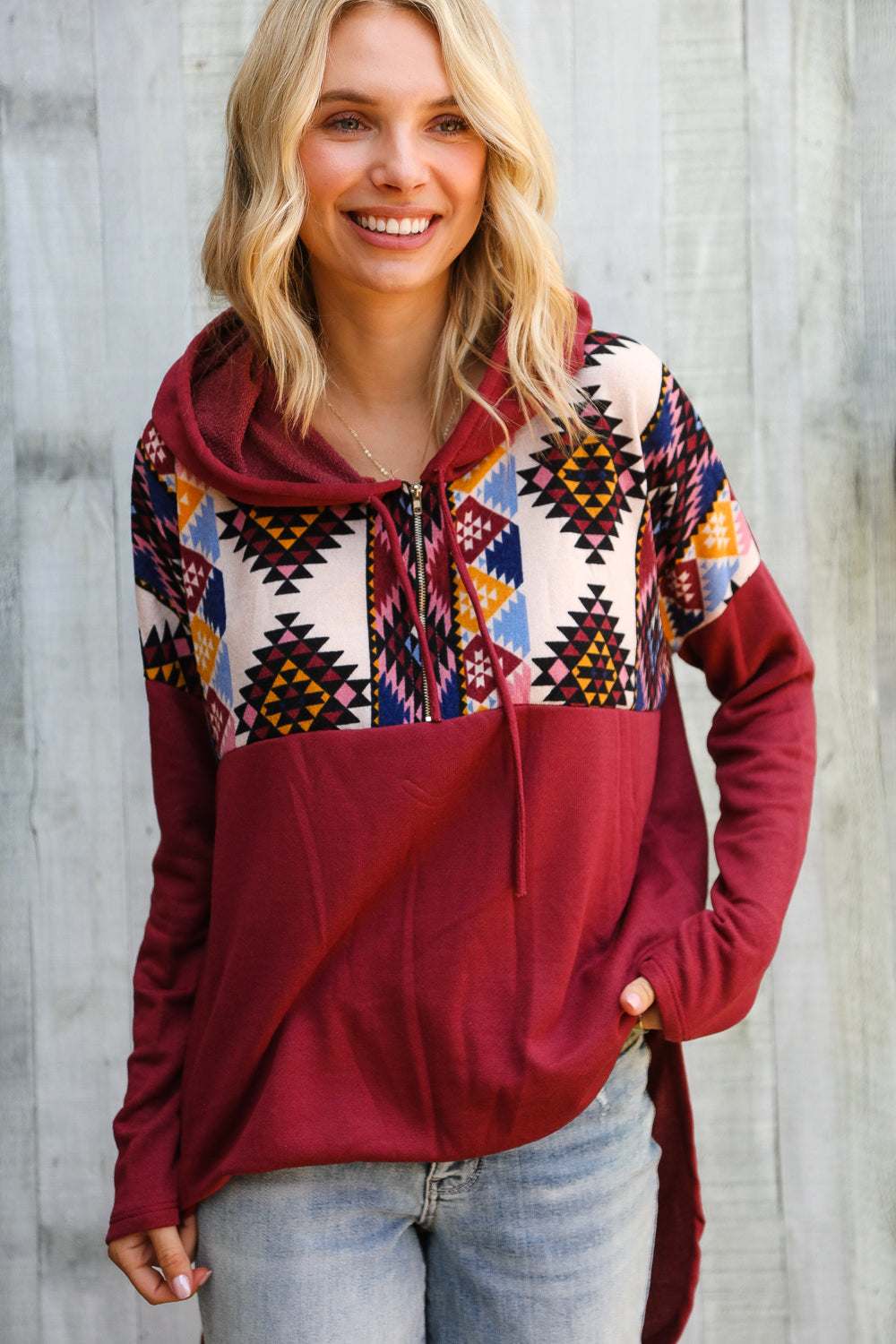 Woman wearing a colorful patterned hoodie with a red base against a wooden background