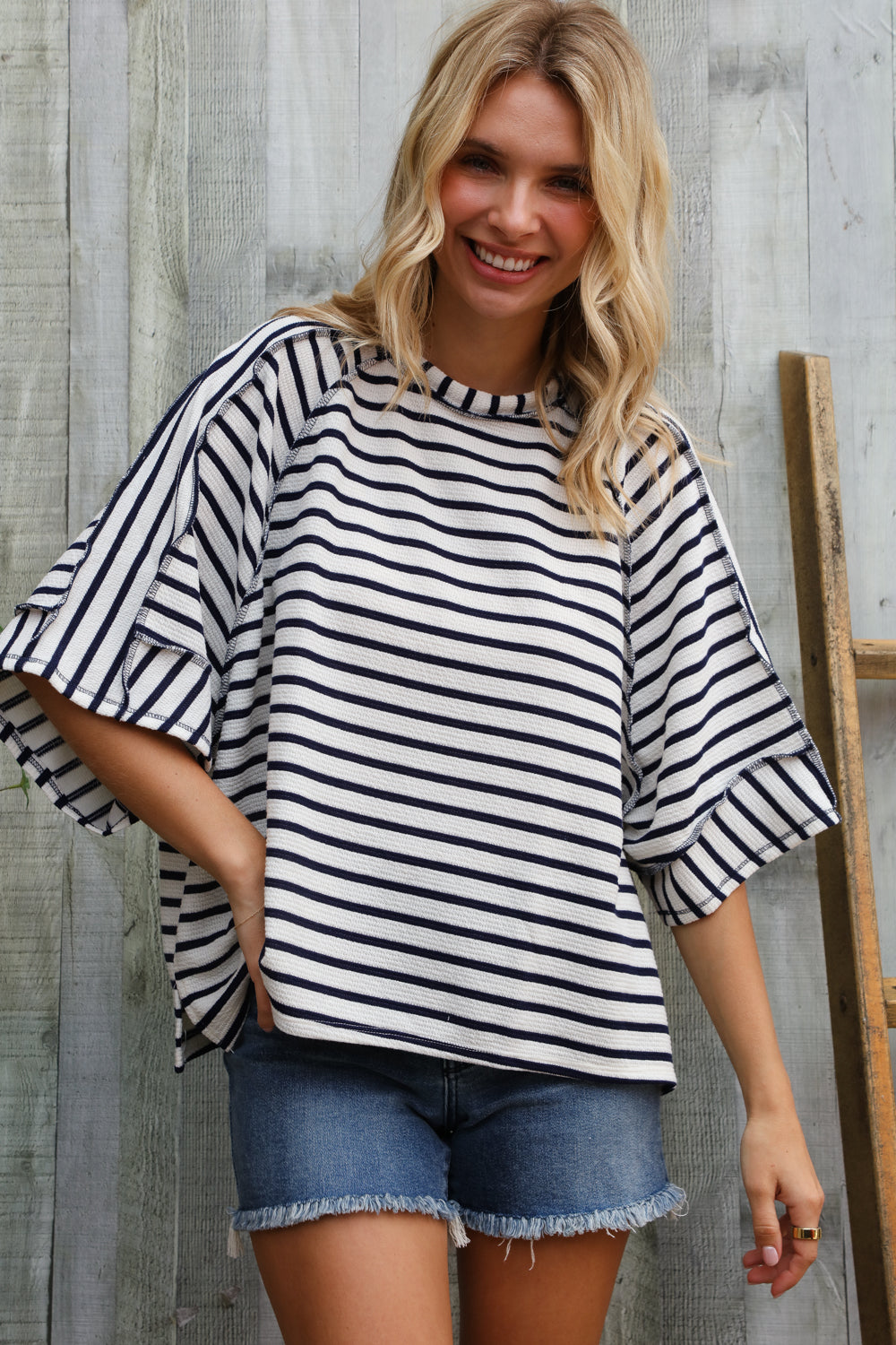 Woman wearing a black and white striped shirt and denim shorts standing against a wooden background