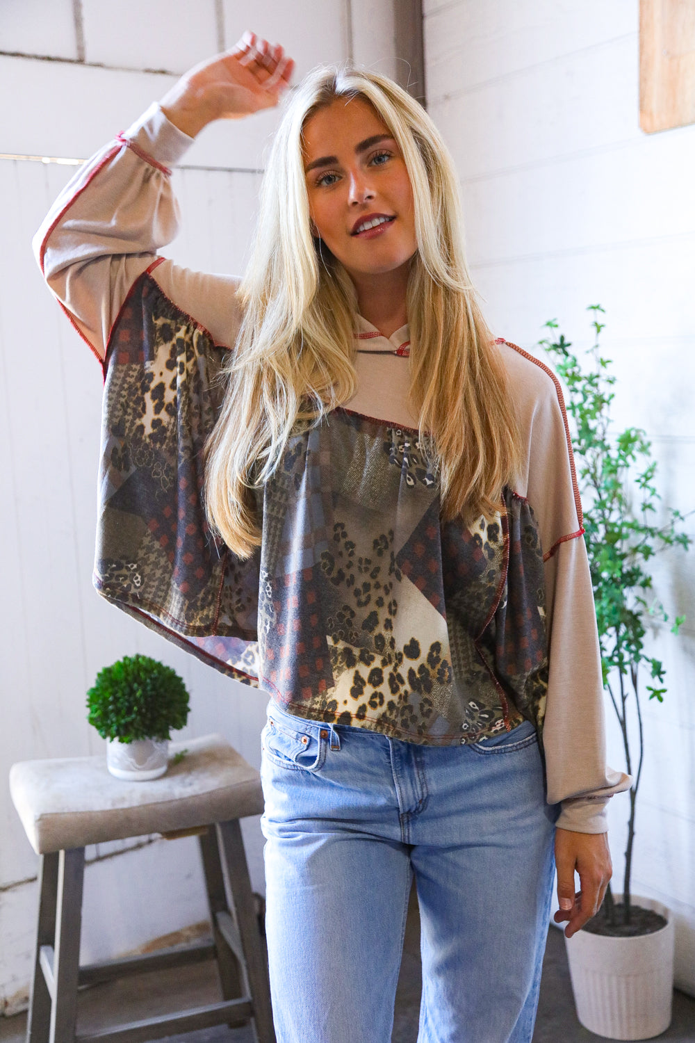 Woman wearing a patterned hoodie top and jeans indoors with plants in the background