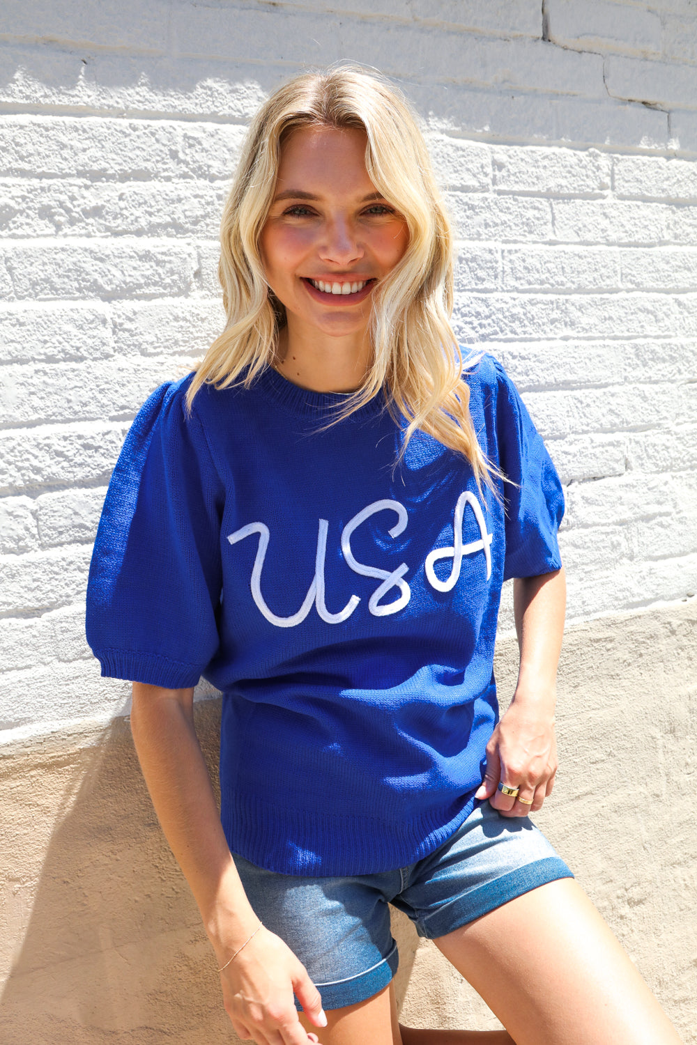 Woman wearing a blue 'USA' t-shirt against a light gray wall.
