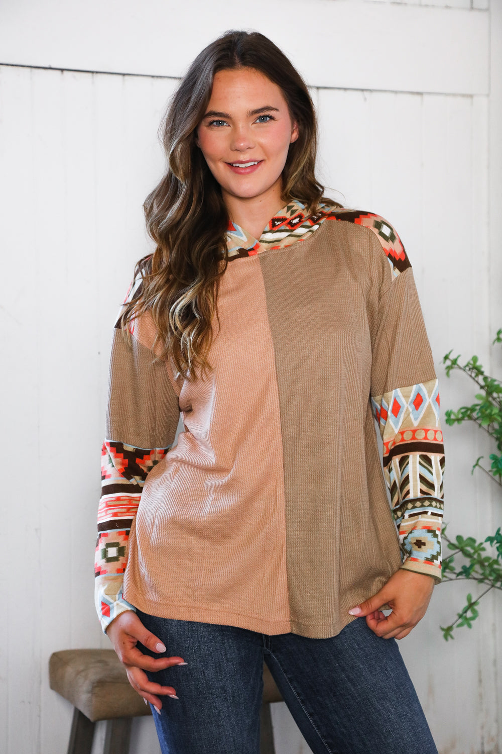 Woman wearing a patterned hoodie top with a neutral color palette against a white wall.