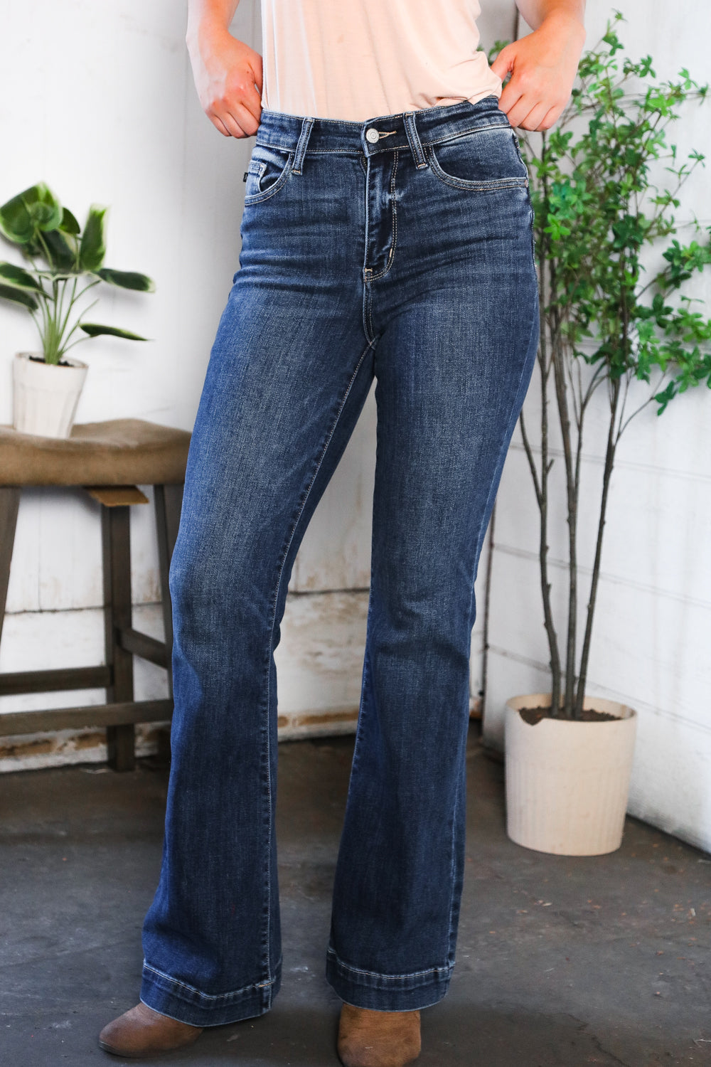 Person wearing blue jeans standing in a room with plants and a wooden table.