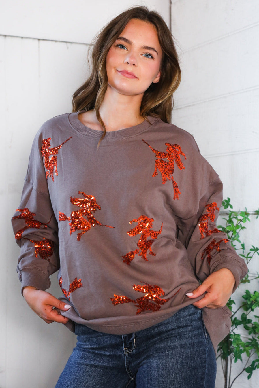 Woman wearing a brown sweatshirt with red sequin embellishments against a white wall.