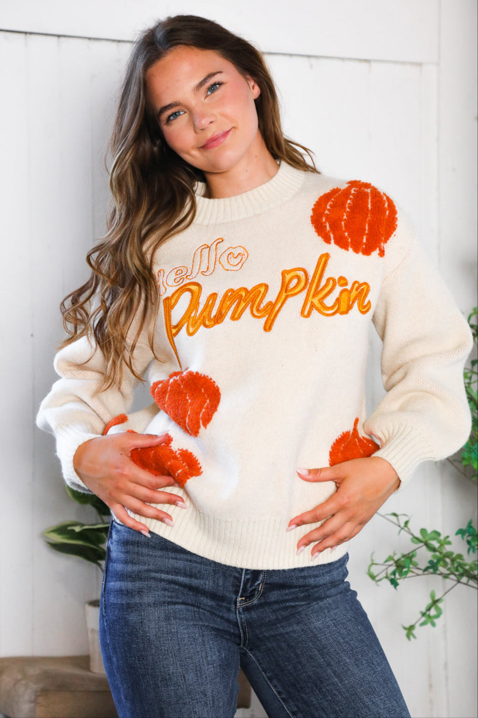 Woman wearing a sweater with 'Hello Pumpkin' text and pumpkin graphics.