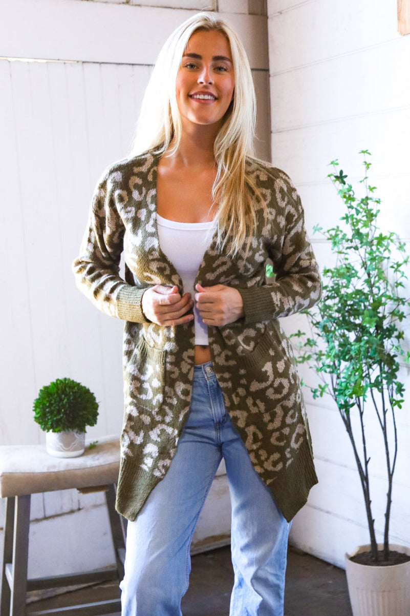 Woman wearing a leopard print cardigan in a home setting with plants and a white wall.