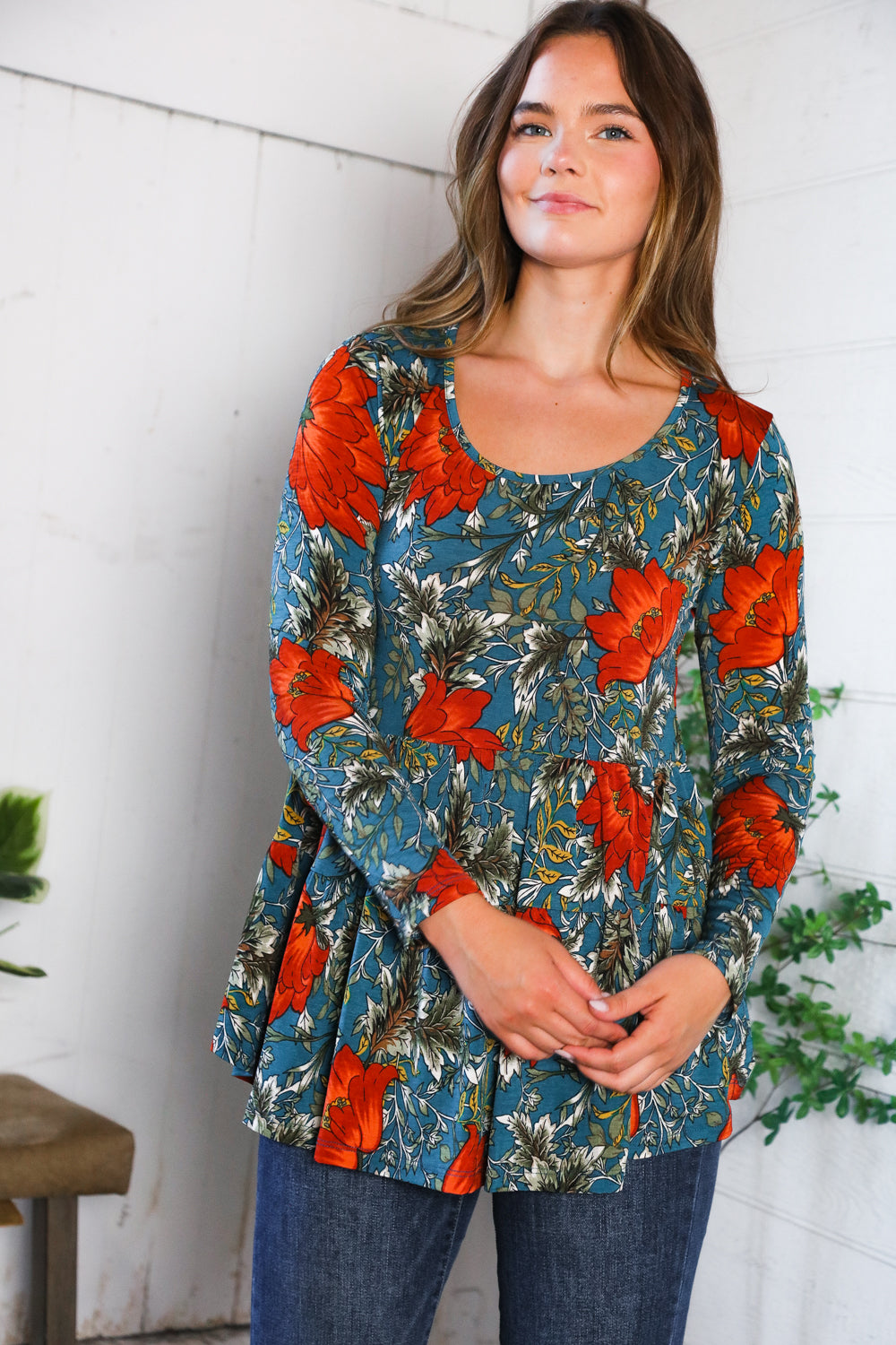 Woman wearing a floral long-sleeve top with orange flowers against a white wall.