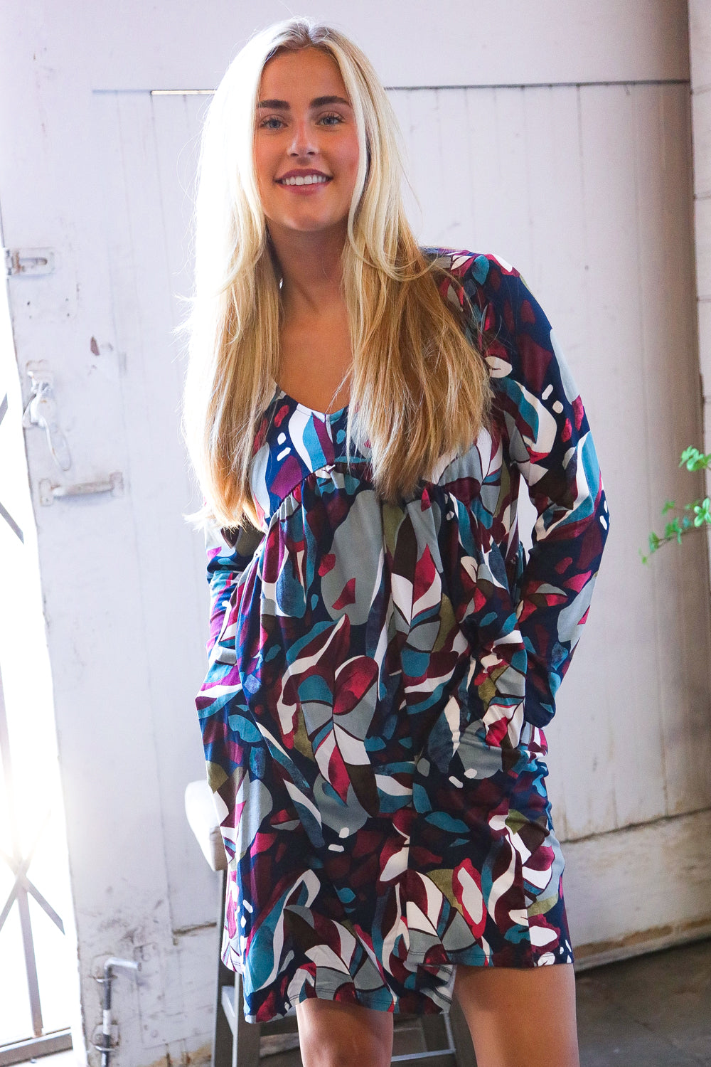 Woman wearing a colorful patterned dress standing against a white wall.