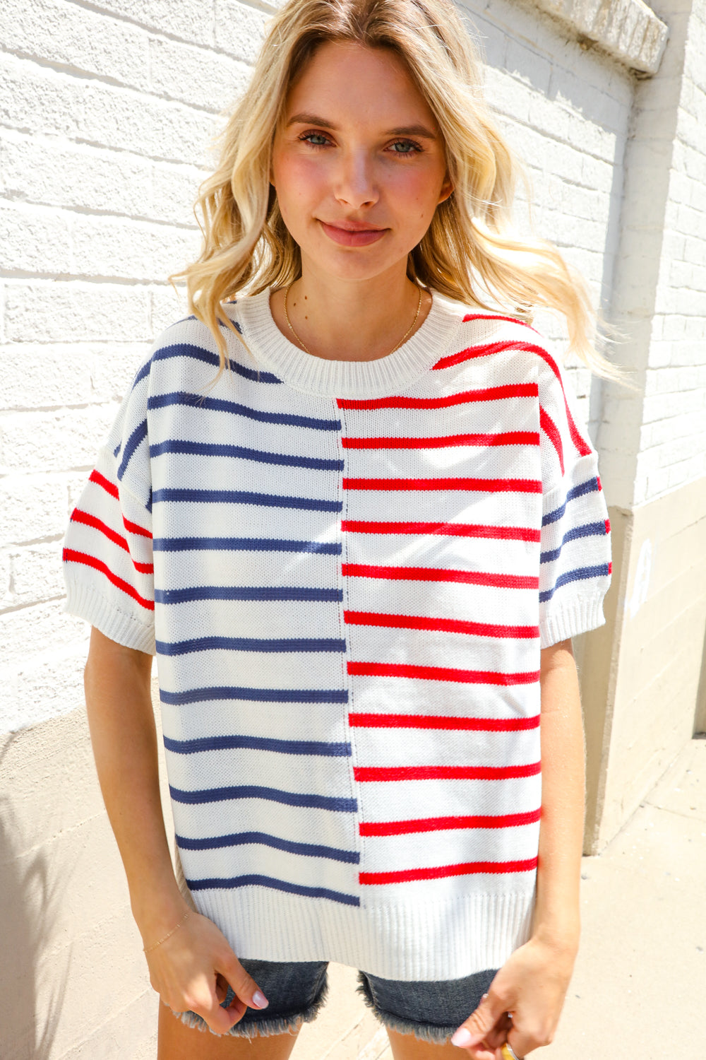 A woman wearing a striped oversized sweater with red, white, and blue colors, with short sleeves and a round neckline.