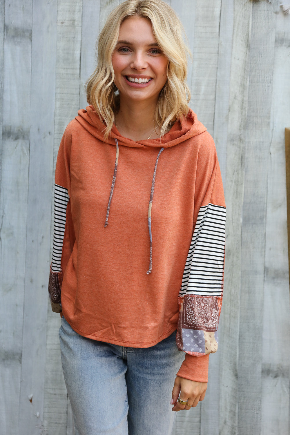 Woman wearing a rust orange-colored hoodie with patterned sleeves against a wooden background