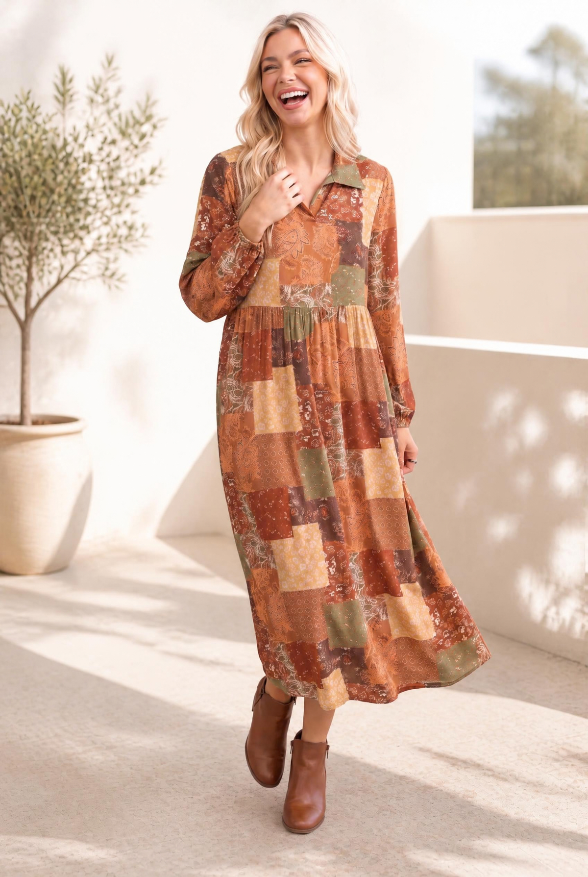 A woman wearing a patchwork midi dress with long sleeves, featuring a mix of browns, greens, and yellows, paired with brown ankle boots.