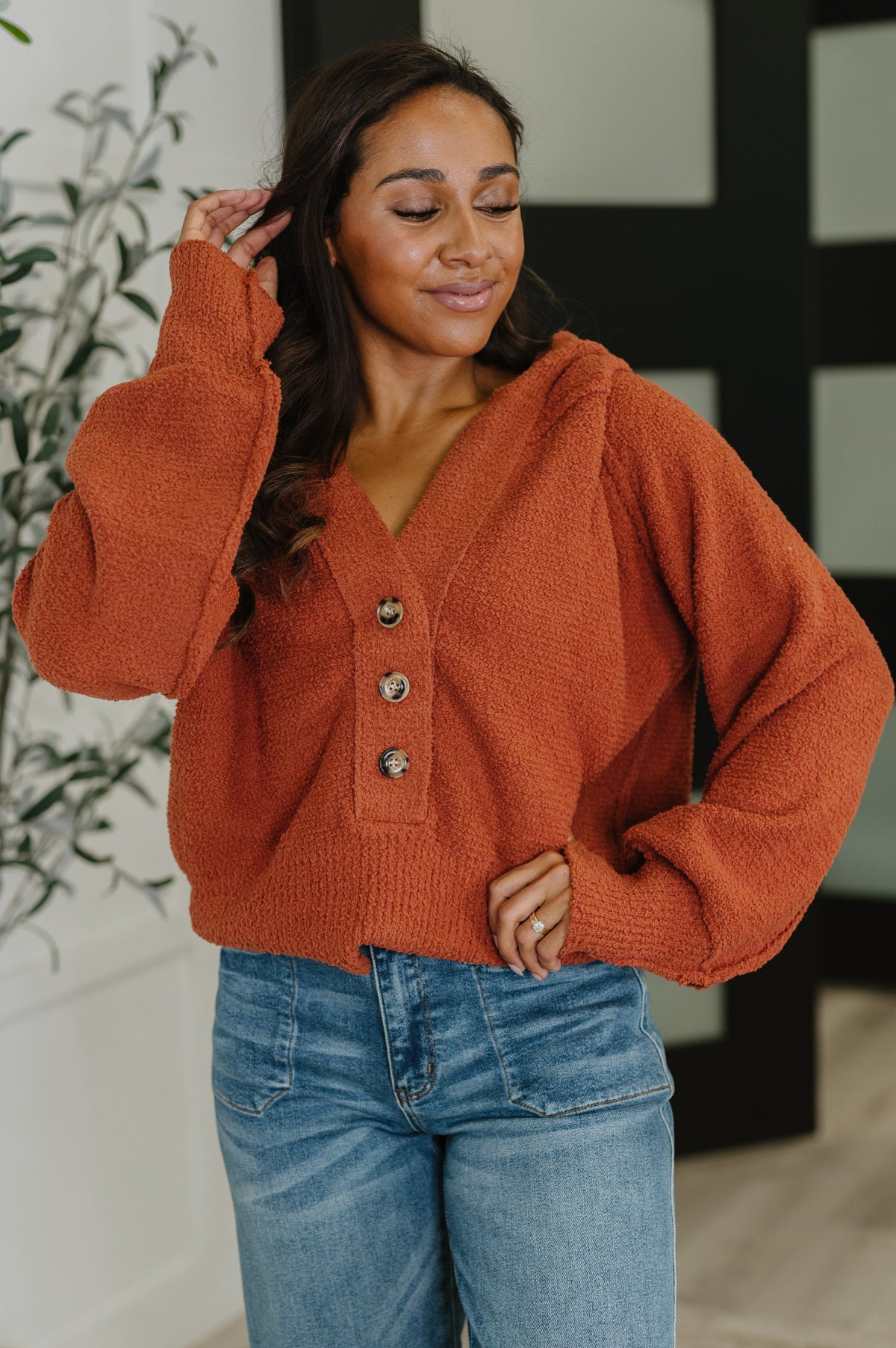 A woman wearing a rust-colored textured Henley sweater with a banded V-neckline and hood.