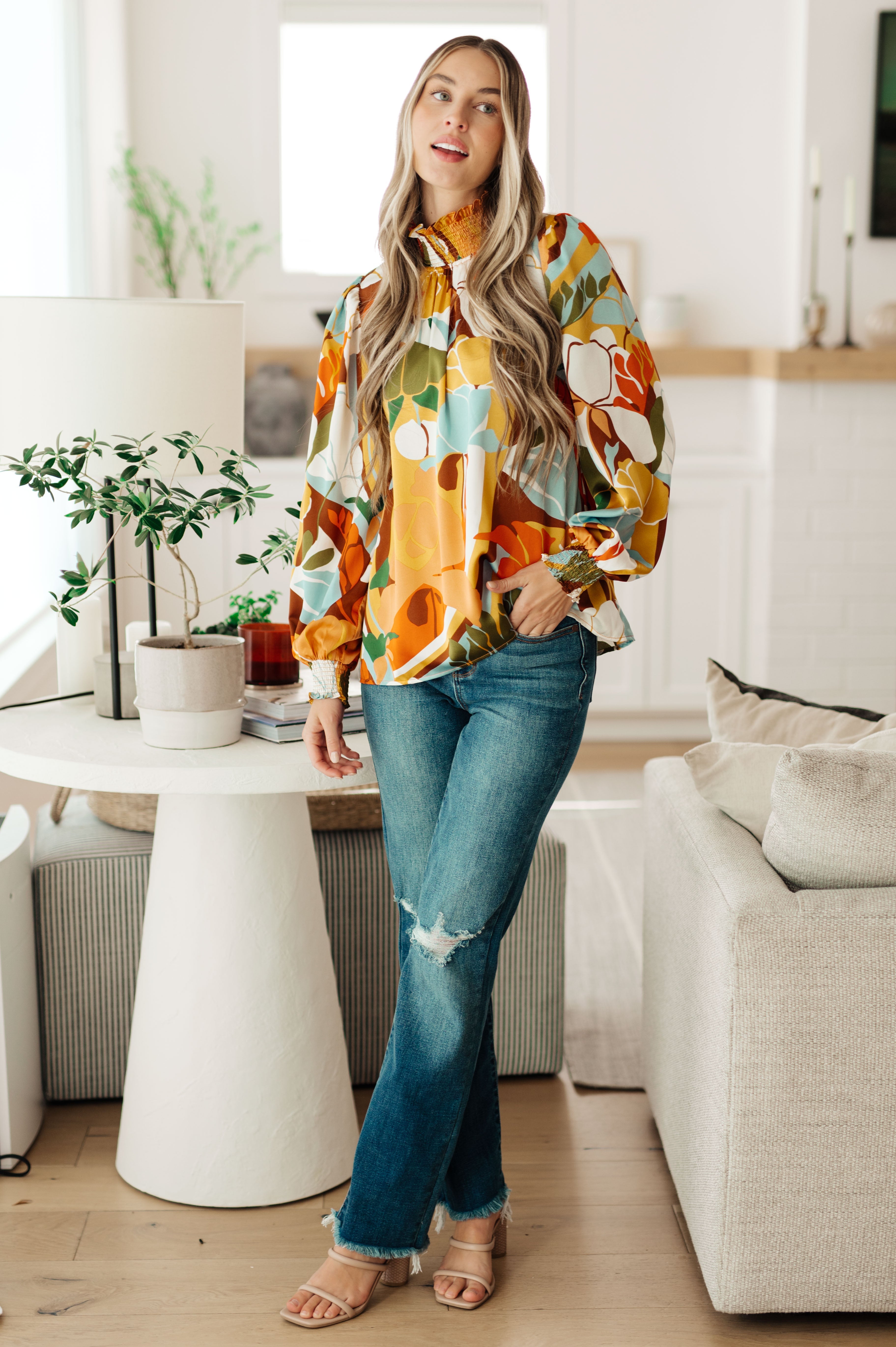 Woman in a colorful shirt and jeans standing in a modern living room.