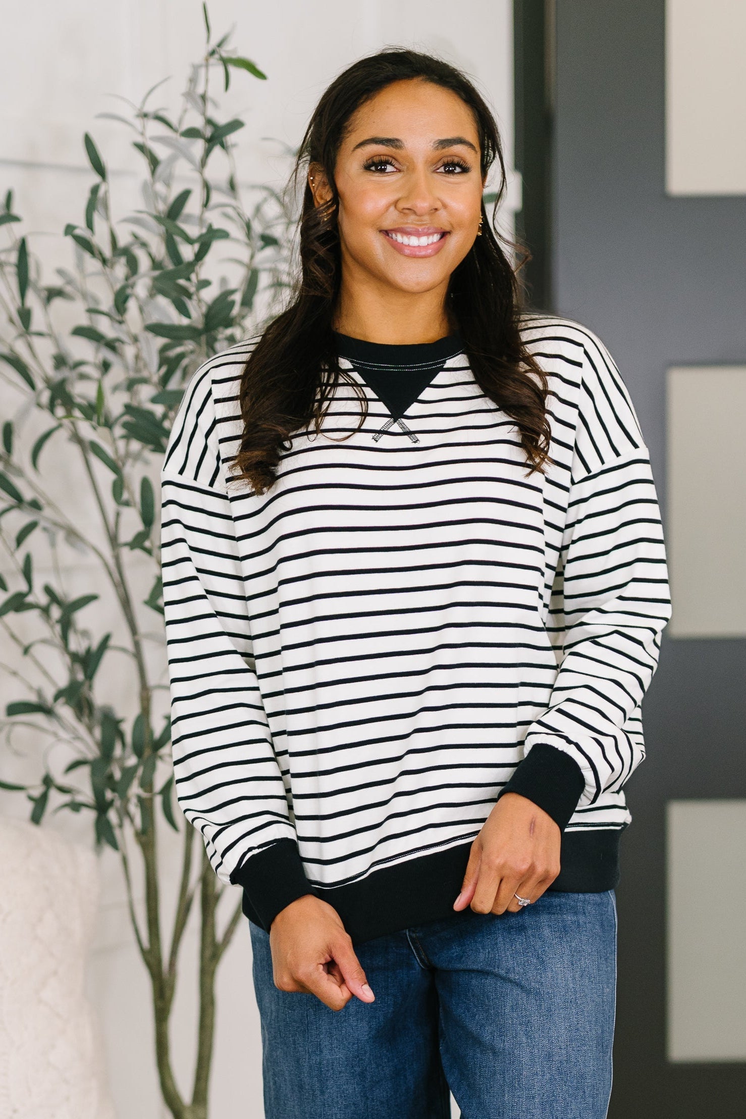 A woman wearing a white and black striped drop shoulder pullover with ribbed cuffs and hemline.