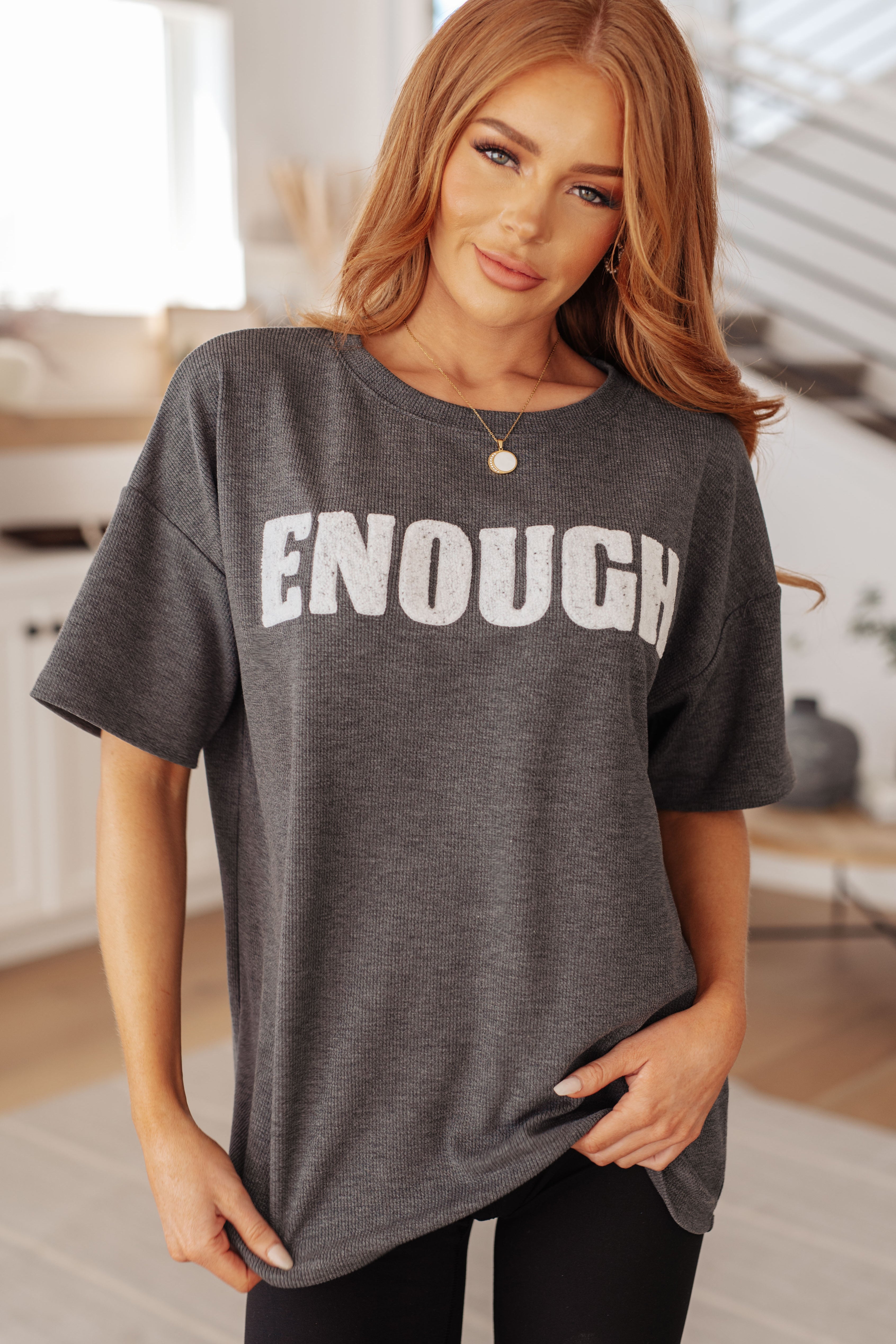 Woman wearing a gray t-shirt with 'ENOUGH' text in a casual setting