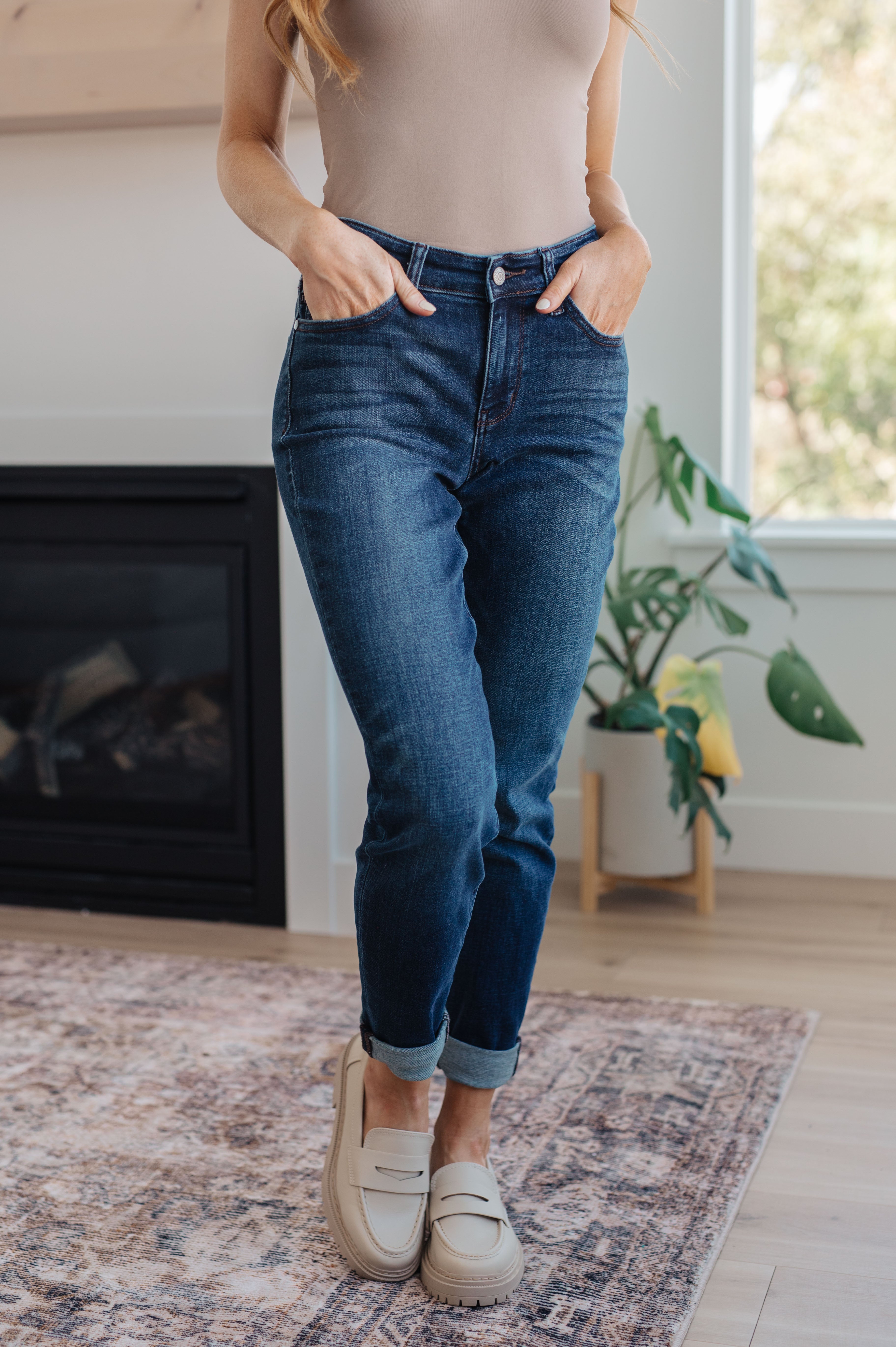 Woman wearing blue jeans and beige shoes in a room with a fireplace and plant.