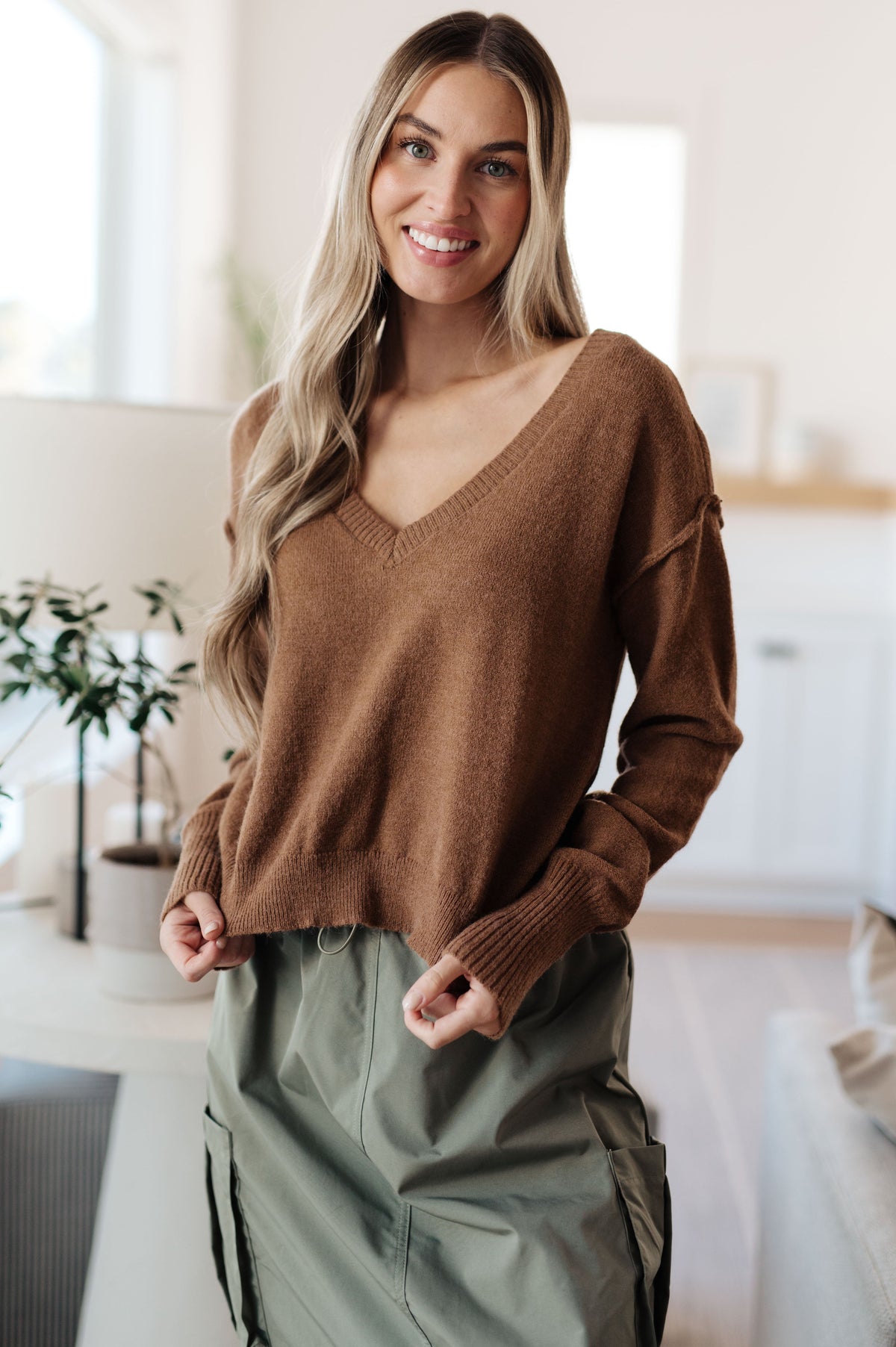 Mocha V-neck sweater with cropped length, exposed seams, and dropped shoulder design worn by a model.