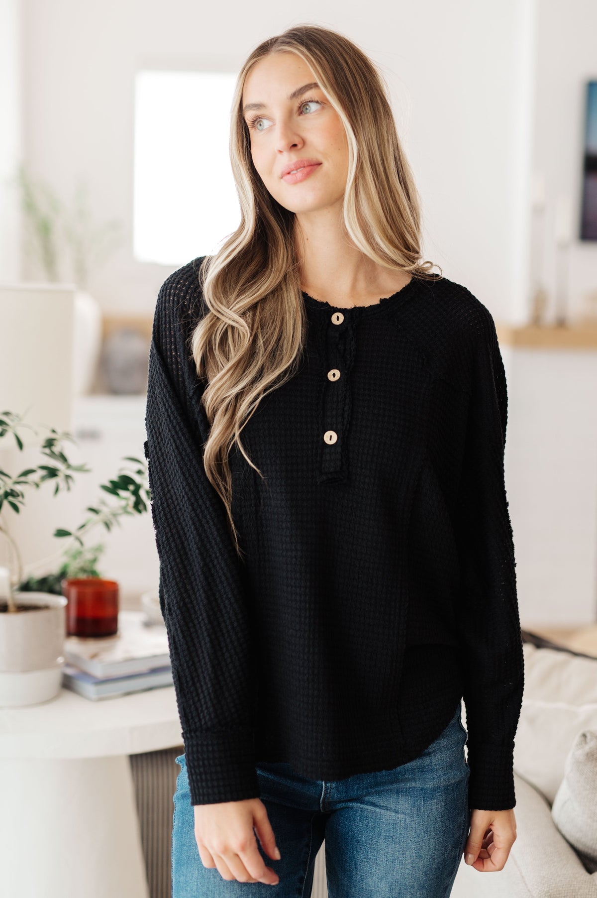 A woman wearing a black waffle knit Henley top with wooden buttons.