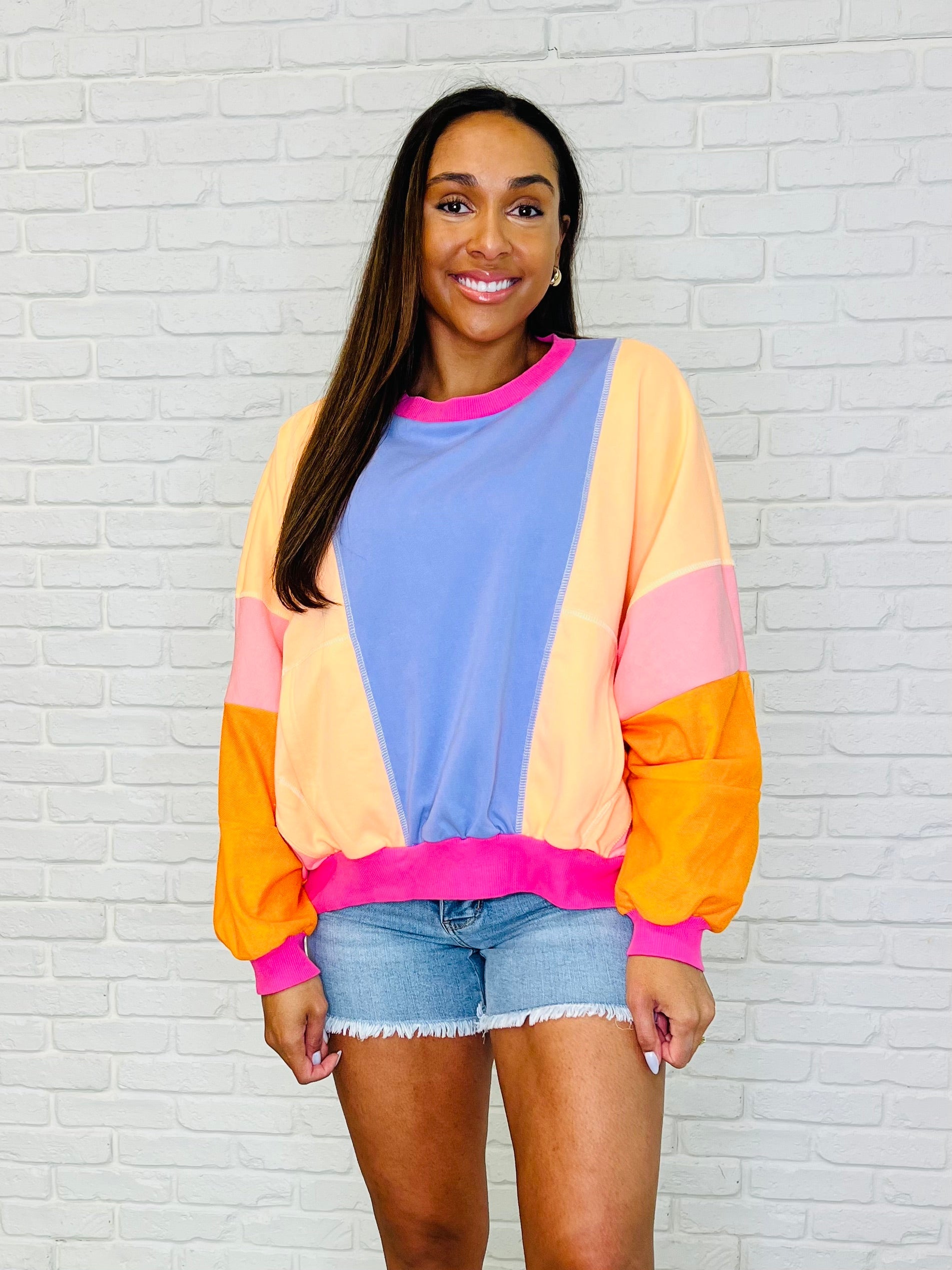 A woman wearing a color block pullover with dolman sleeves and ribbed cuffs, in shades of blue, pink, orange, and purple.