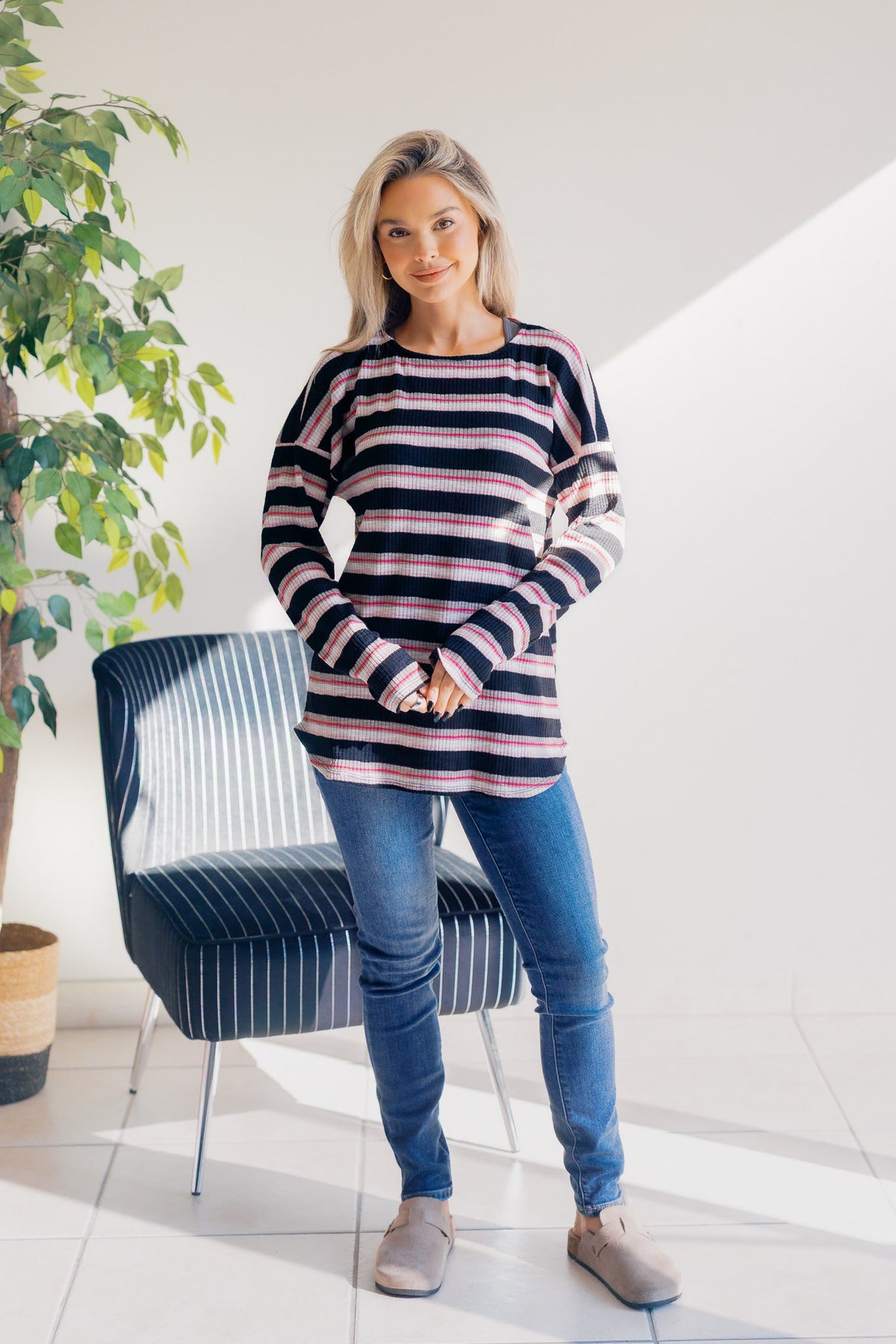 Pullover with black, pink, and white stripes, featuring a round neckline and rounded hem.