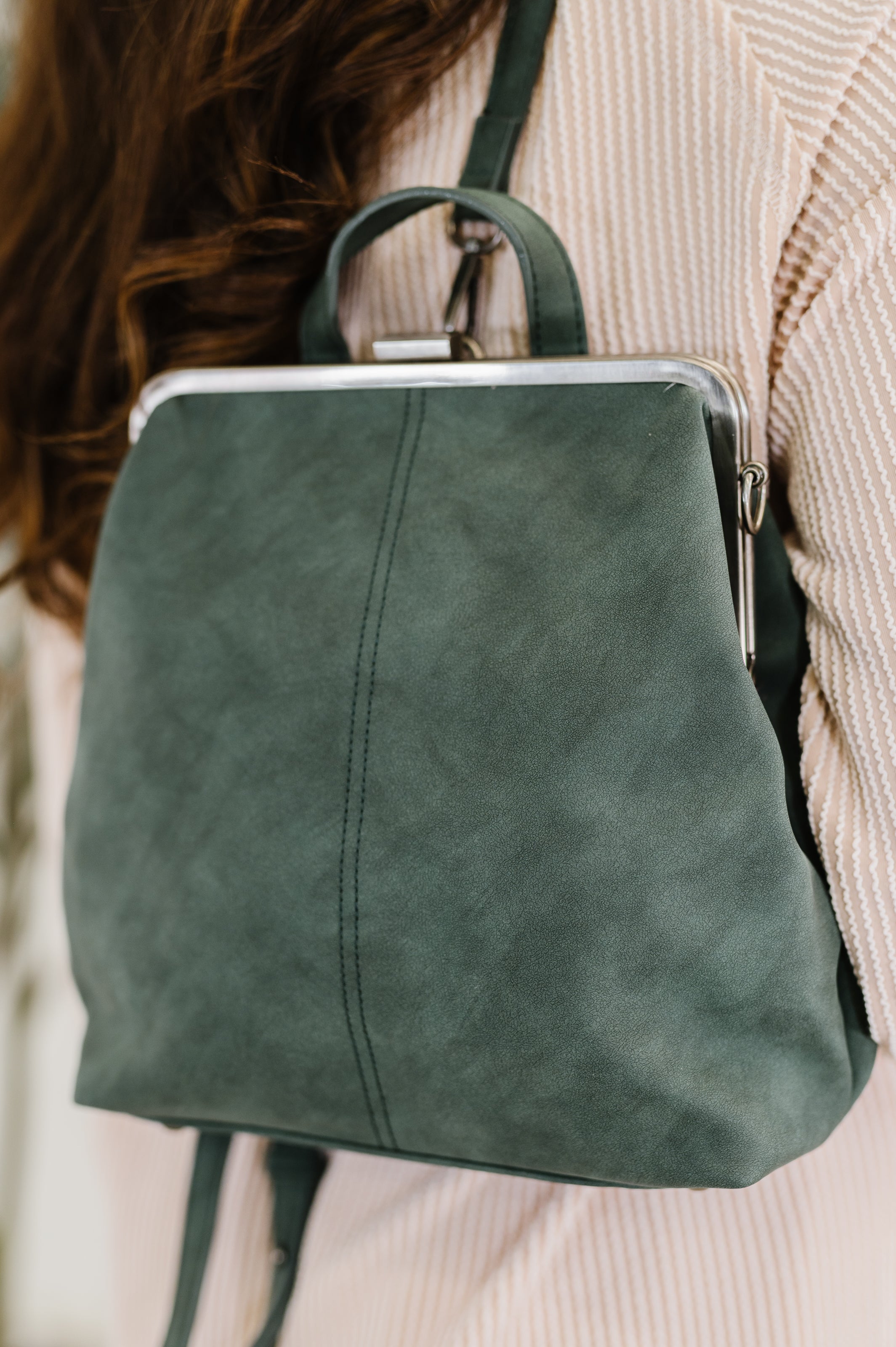 Green leather backpack worn by a woman with a blurred background