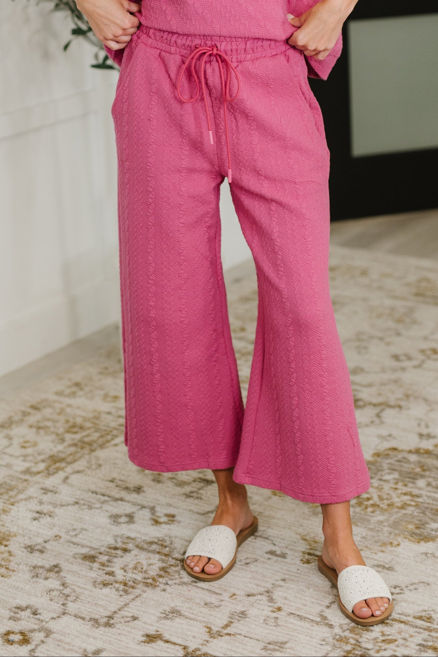 Women wearing bright pink pants with a drawstring waist on a textured floor.