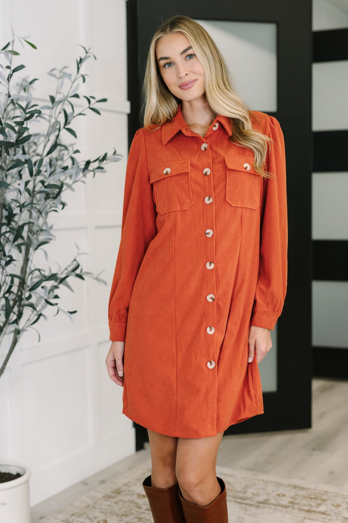 Woman wearing an orange corduroy shirt dress with button-down front and patch pockets.