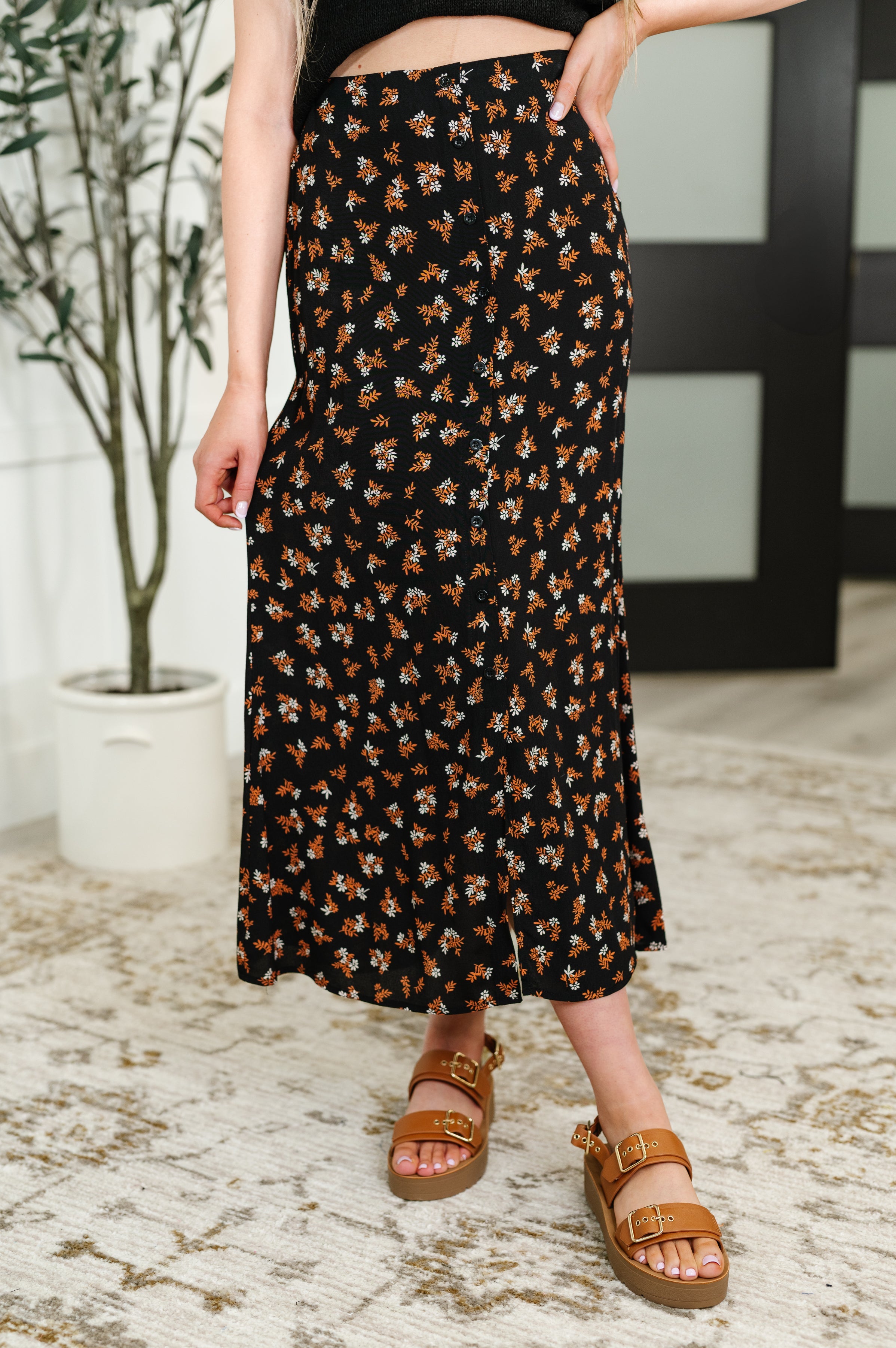 Person wearing a floral patterned skirt with brown sandals on a light floor.