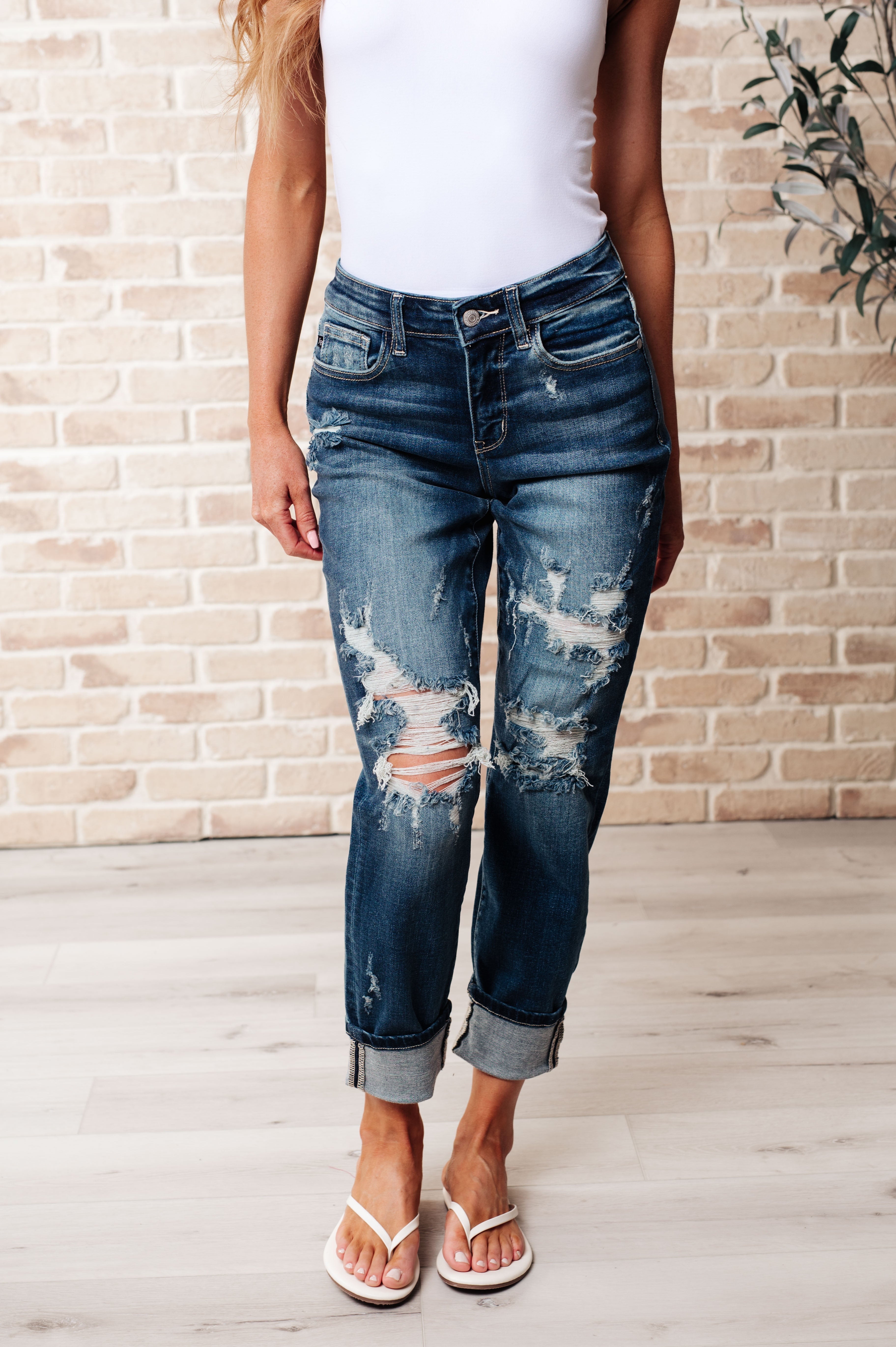 Woman wearing distressed blue jeans and a white top against a brick wall.
