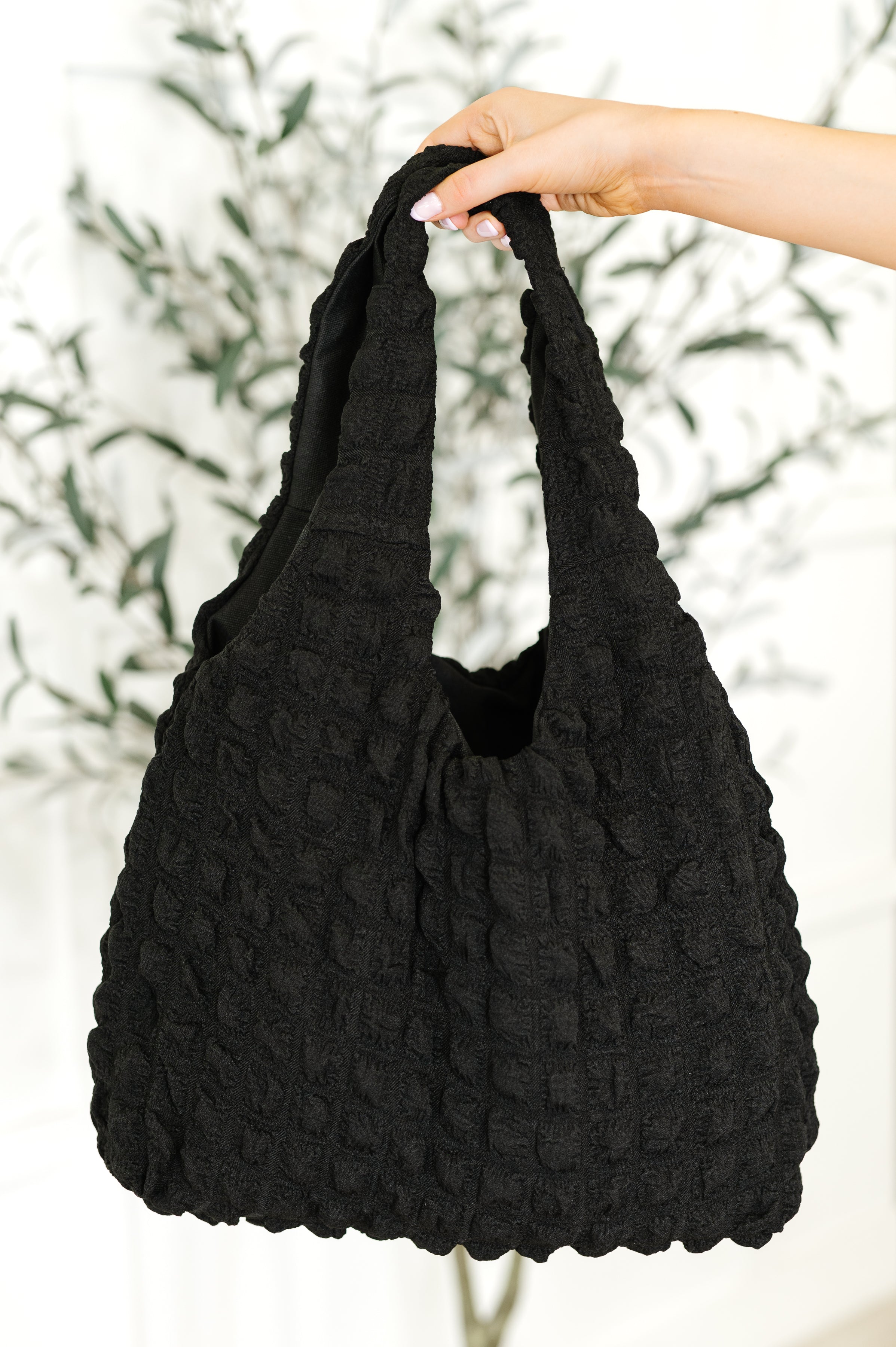 Black textured handbag held by a hand against a blurred natural background