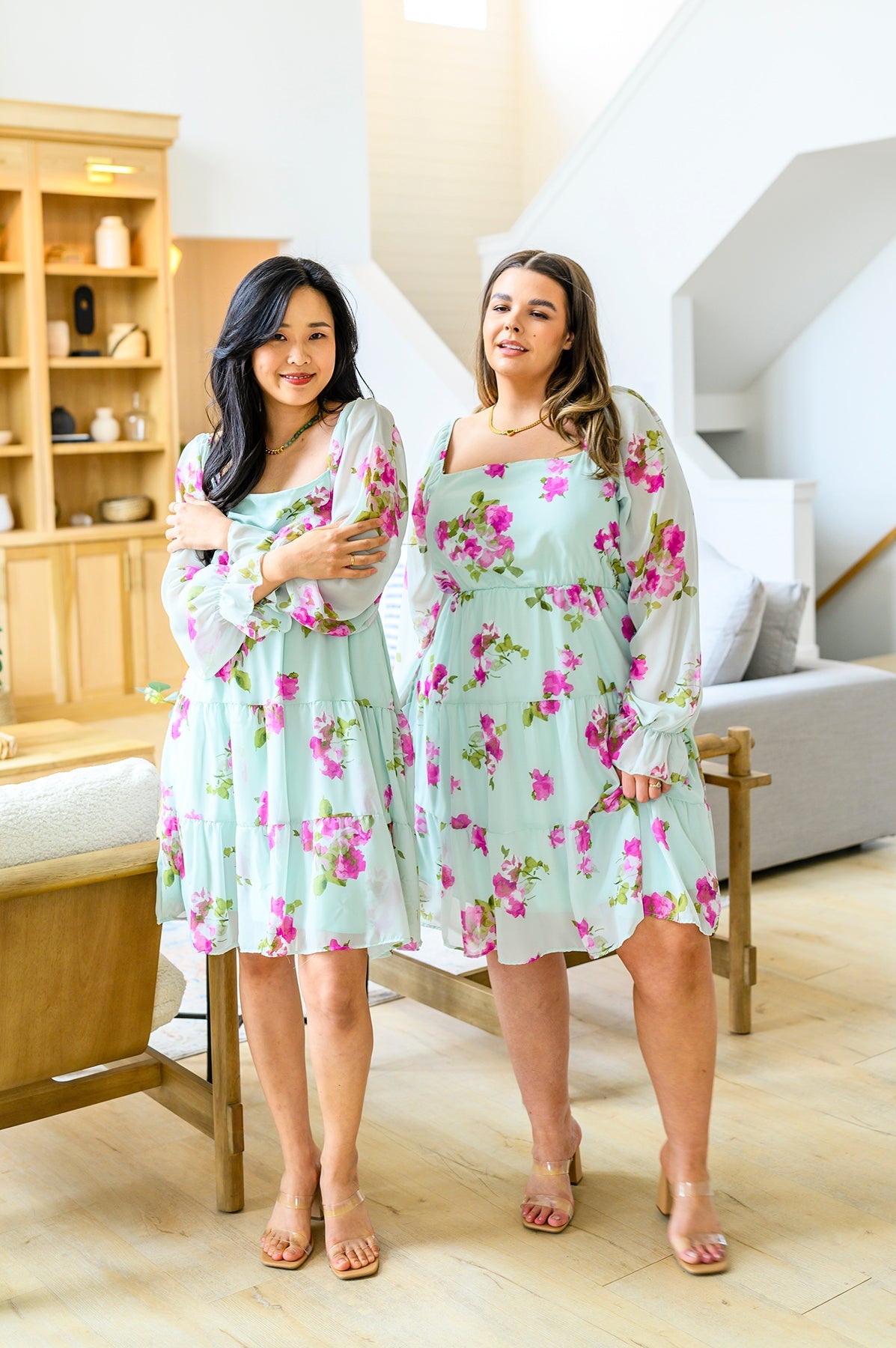Two women wearing floral dresses standing in a living room.