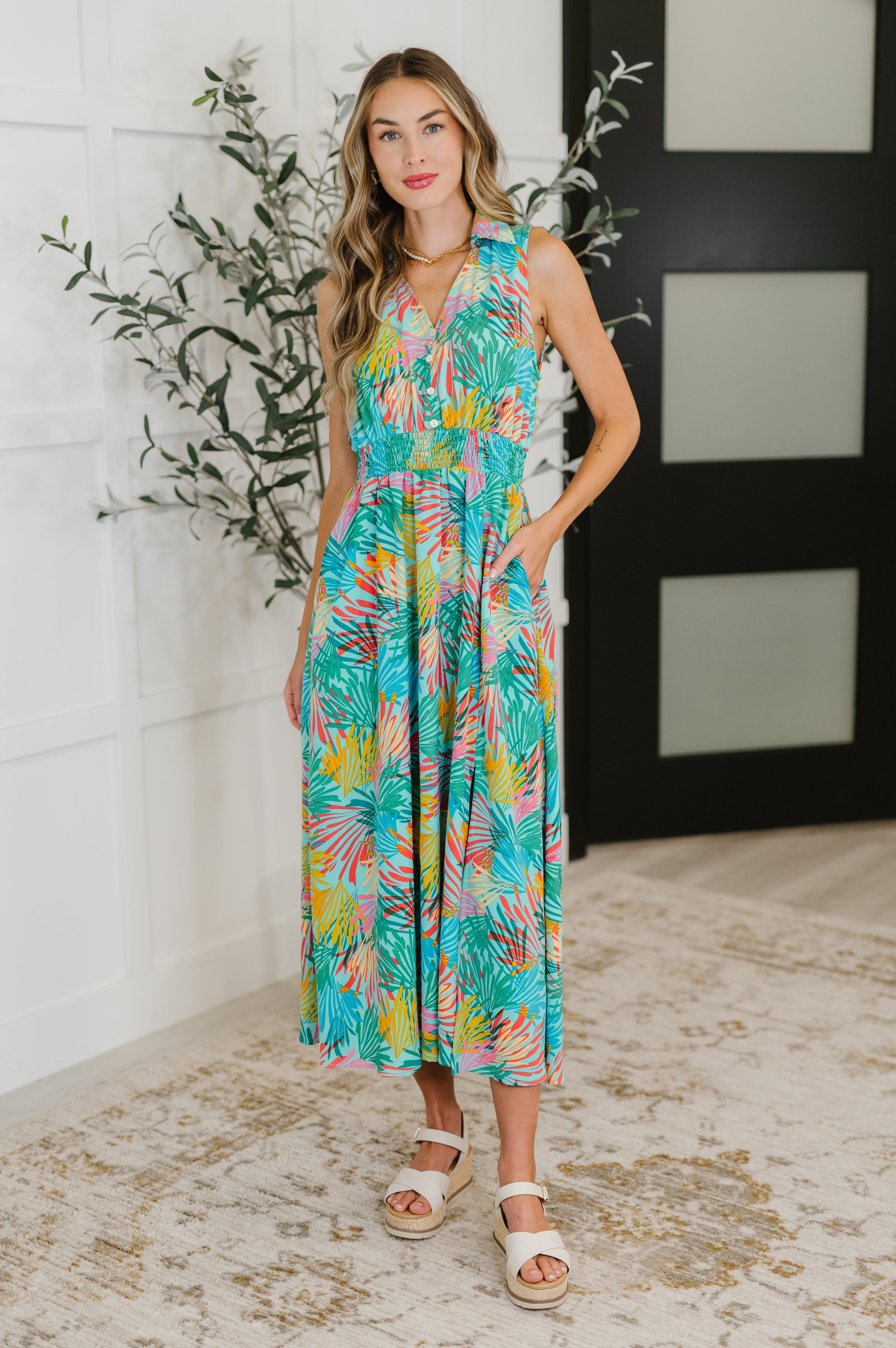 Woman wearing a colorful floral dress standing indoors with a plant in the background