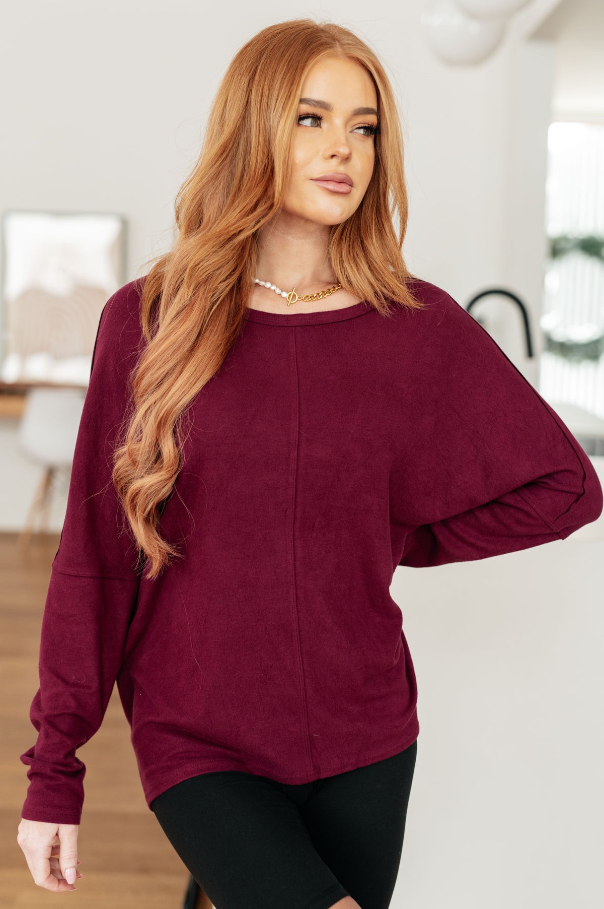 A woman wearing a wine-colored dolman sleeve top with a round neckline and center front seam.