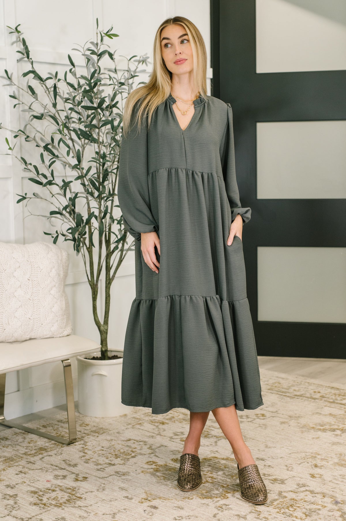 A model wearing a charcoal V-neck tiered dress with long sleeves and a high ruffle neckline.