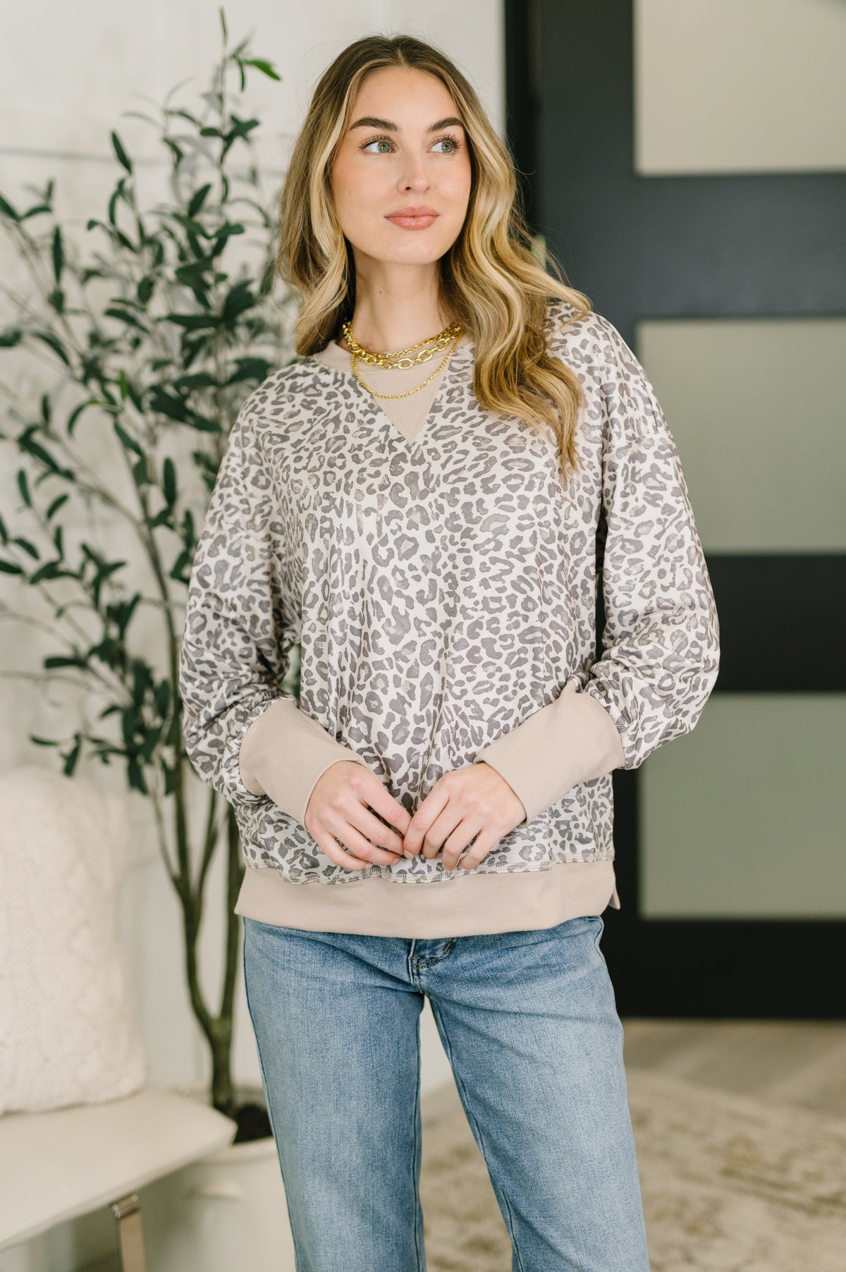 Woman wearing a grey leopard print pullover with a ribbed crew neck and drop shoulders.