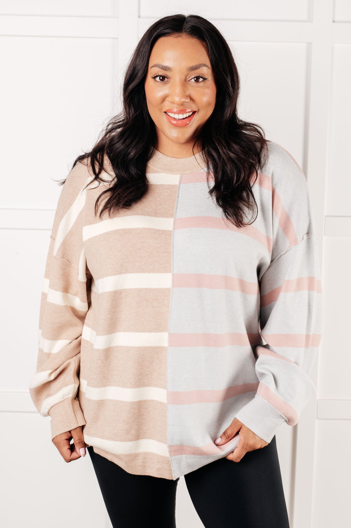 A woman wearing a striped patchwork sweater with drop shoulders and a banded neckline.