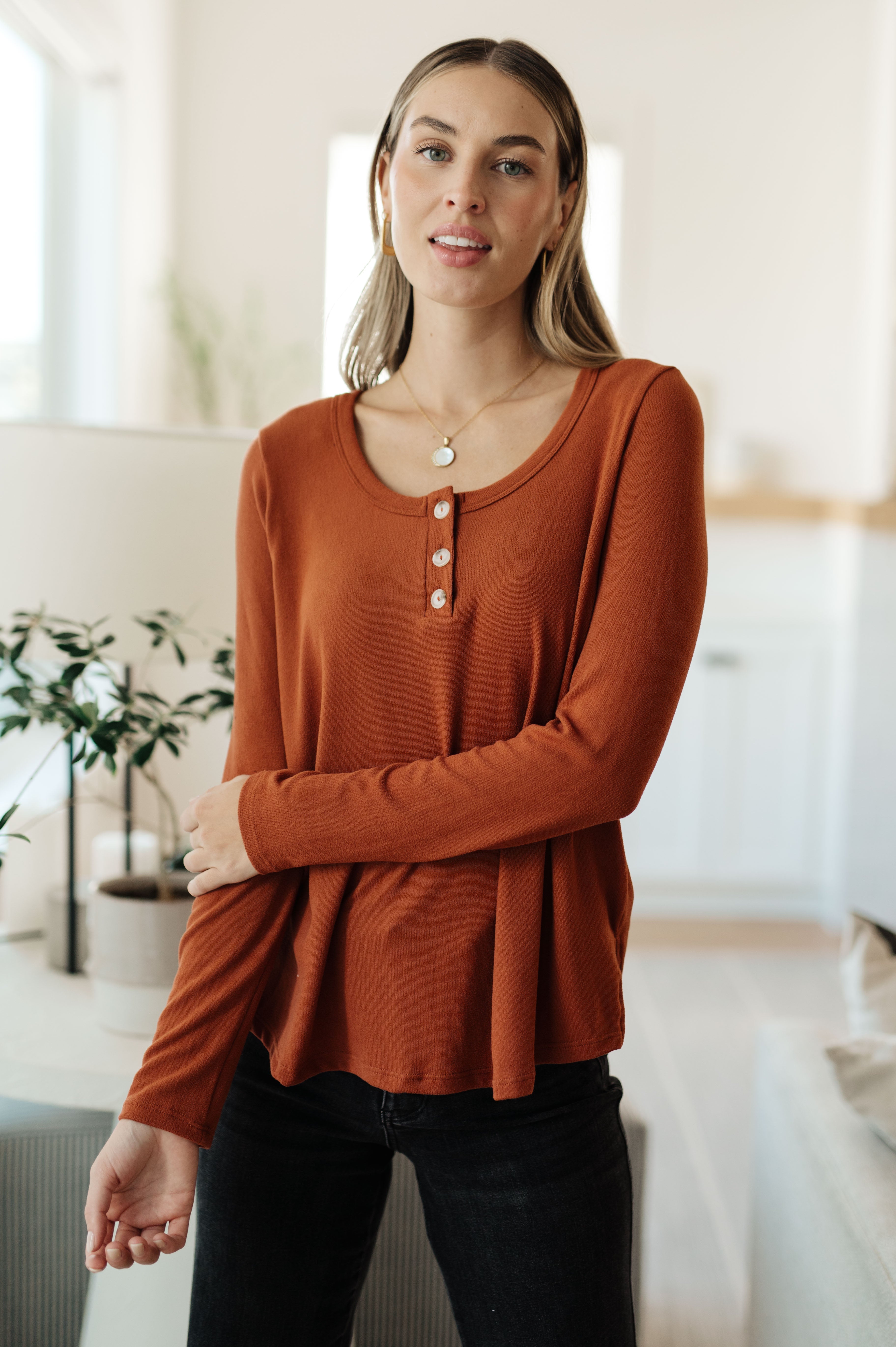 Woman wearing a rust-colored scoop neck top with a button-up Henley design and long sleeves.