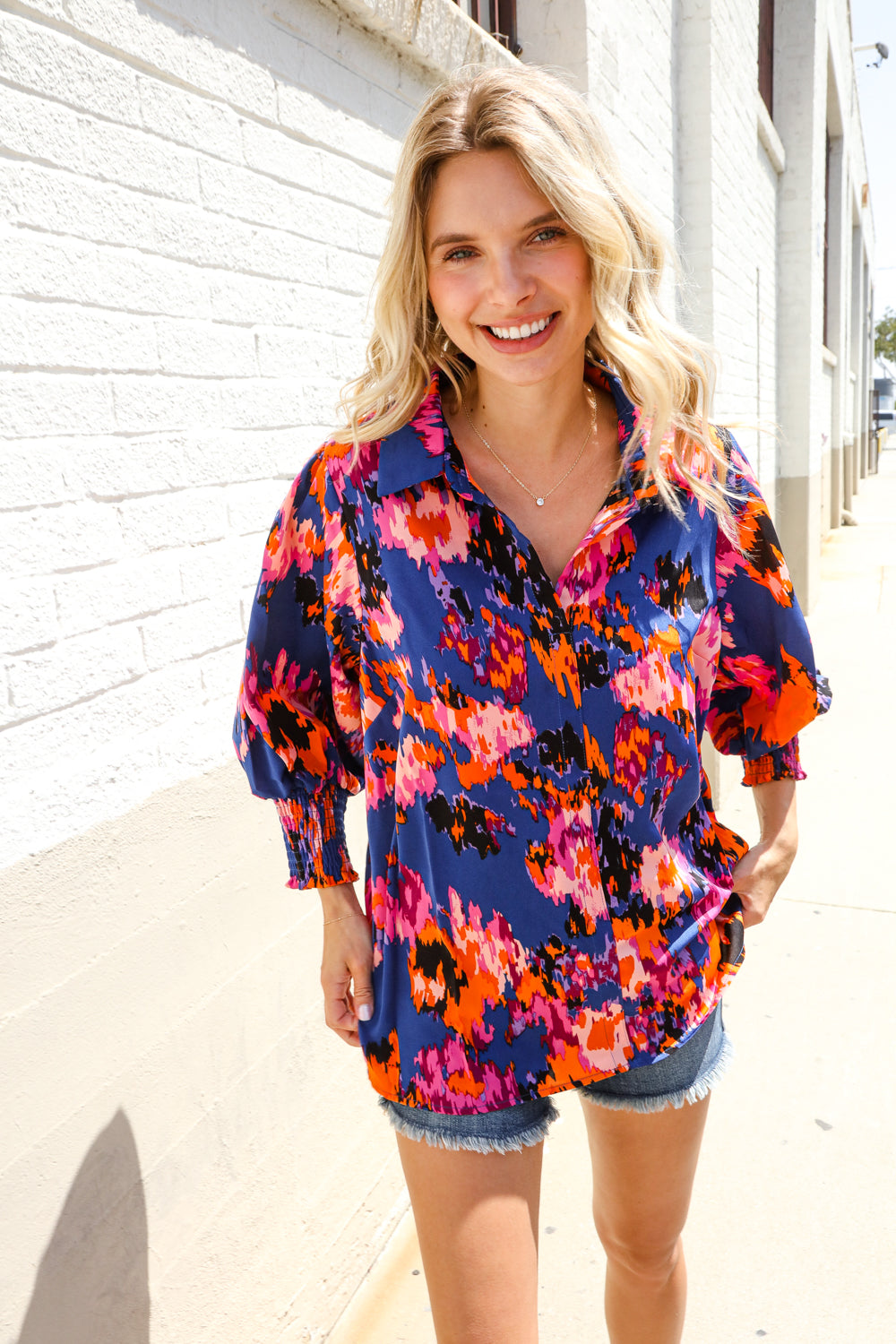 A woman wearing a floral print button-down blouse with smocked sleeves and denim shorts.