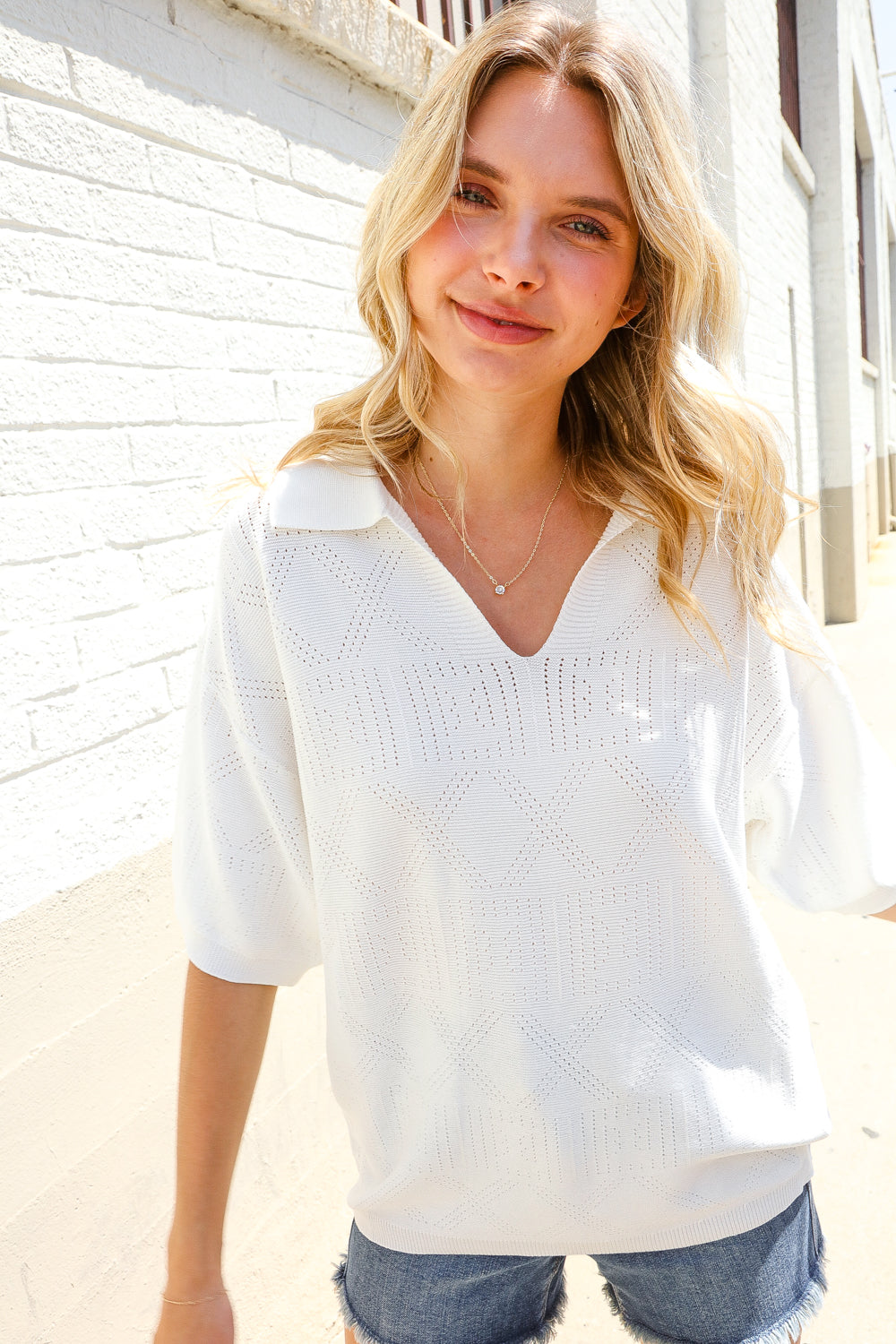 A woman wearing a white collared V neck top with puff short sleeves, paired with blue denim shorts.