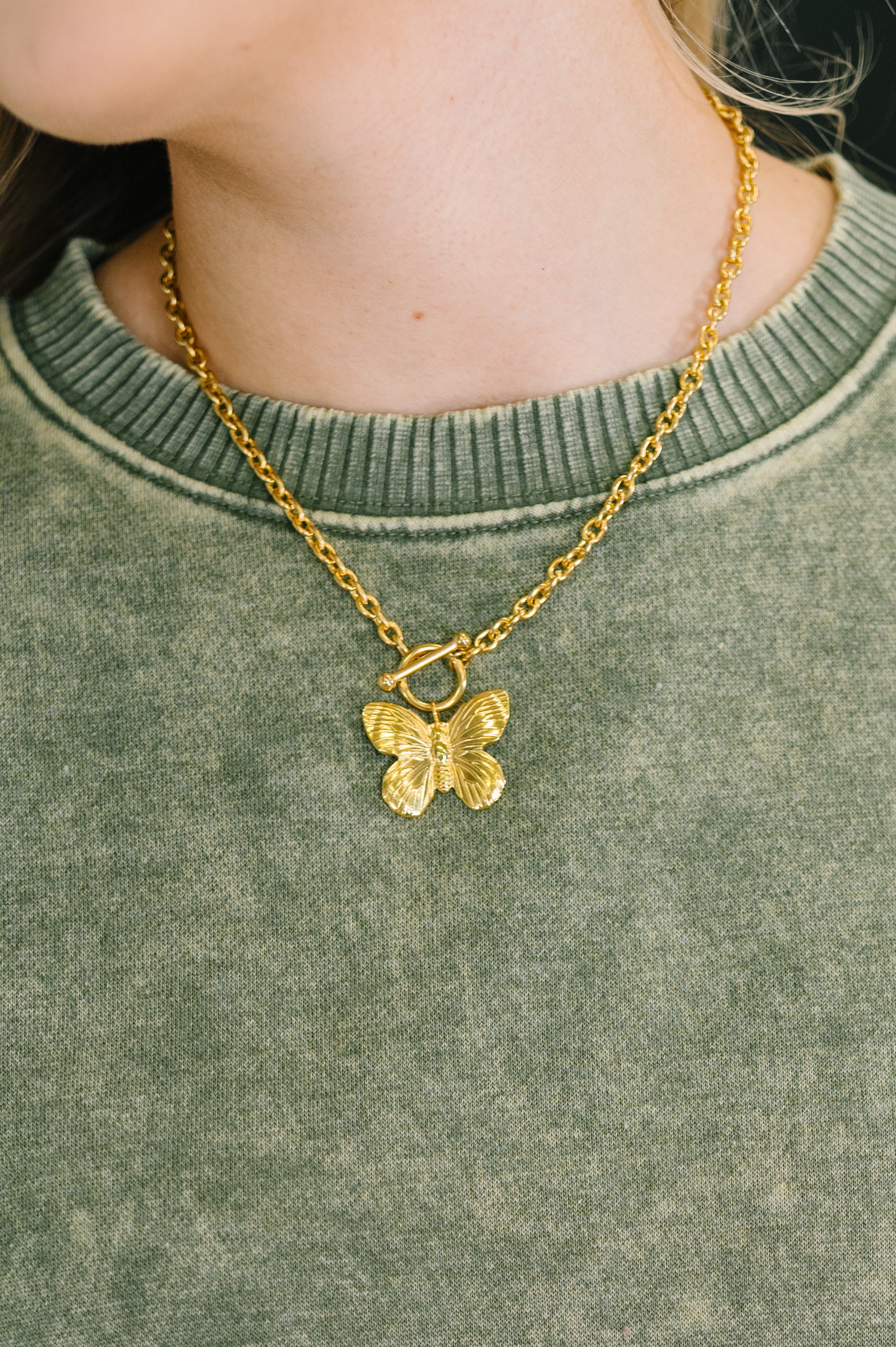 Gold butterfly necklace on a person wearing a green sweater