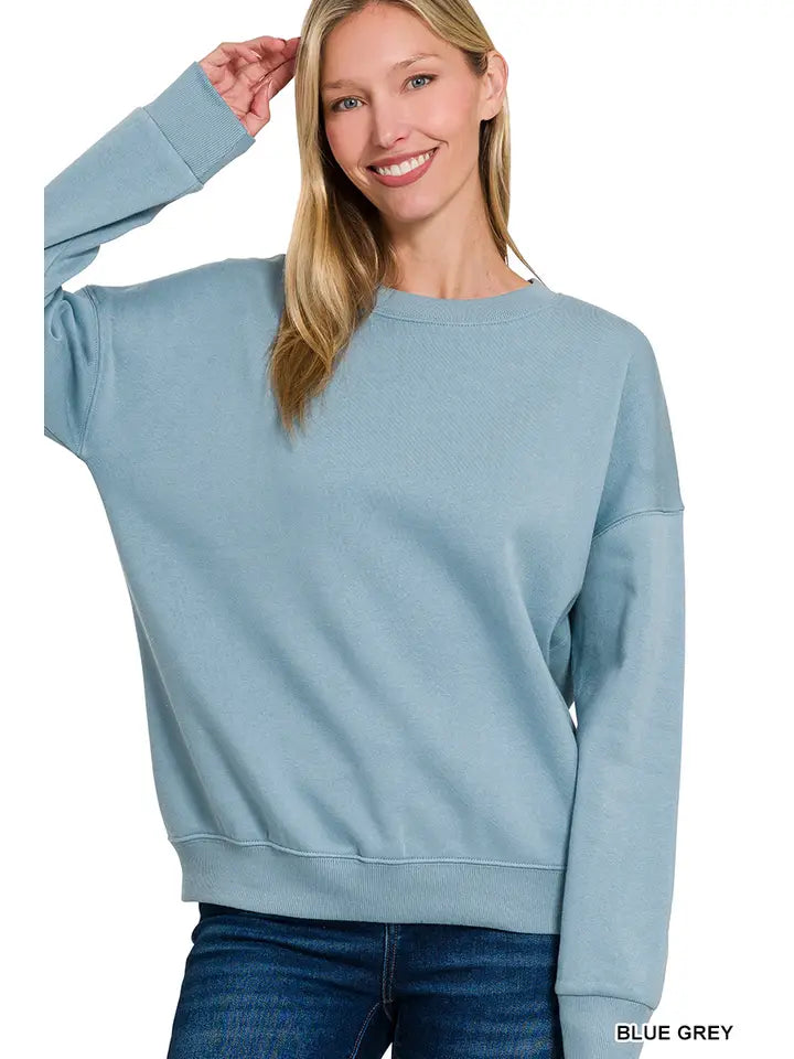 A woman wearing a dusty teal pullover with a relaxed drop shoulder fit and banded neckline.