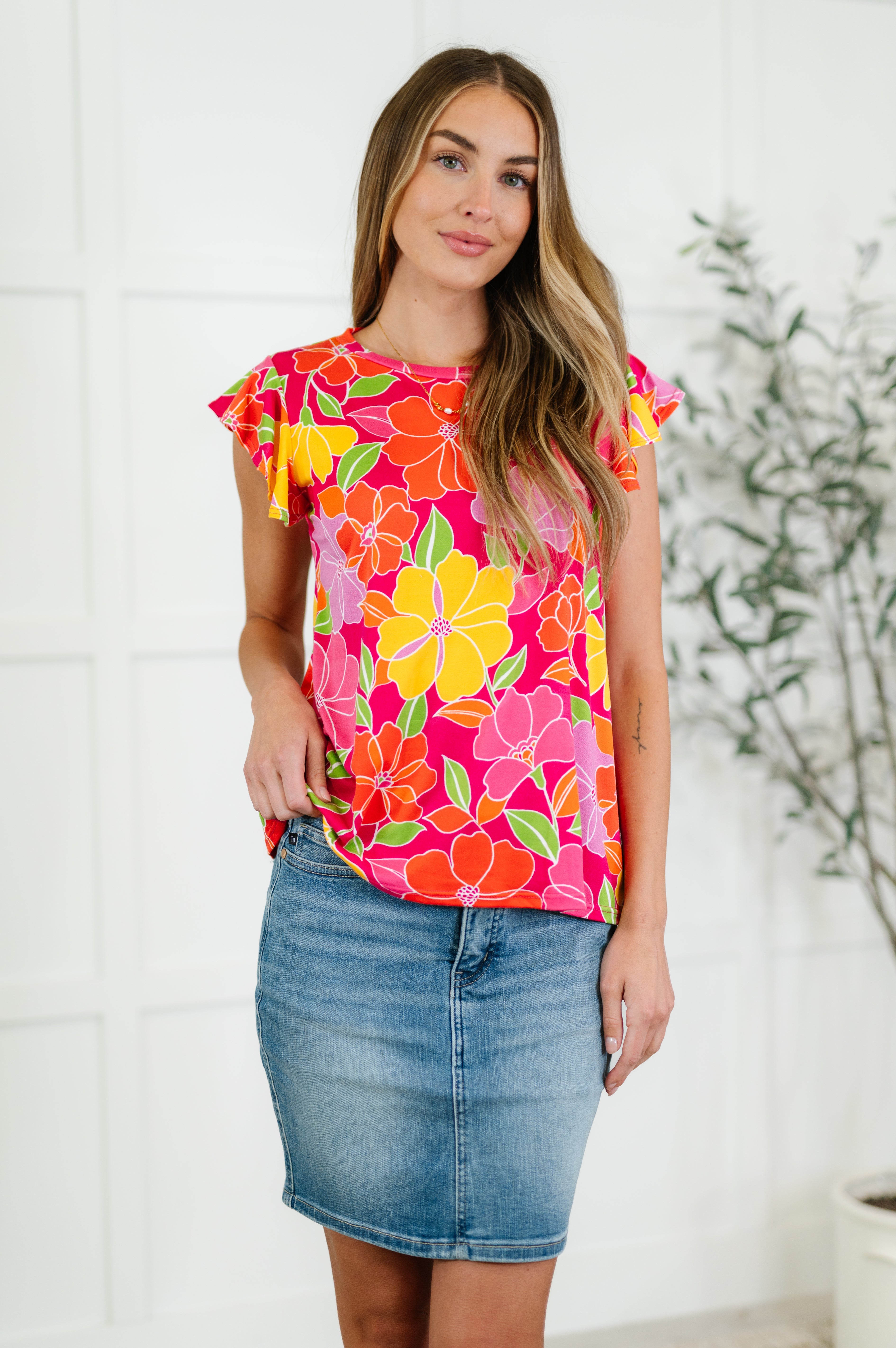 A woman wearing a colorful floral flutter sleeve top with a round neckline, paired with a blue denim skirt.
