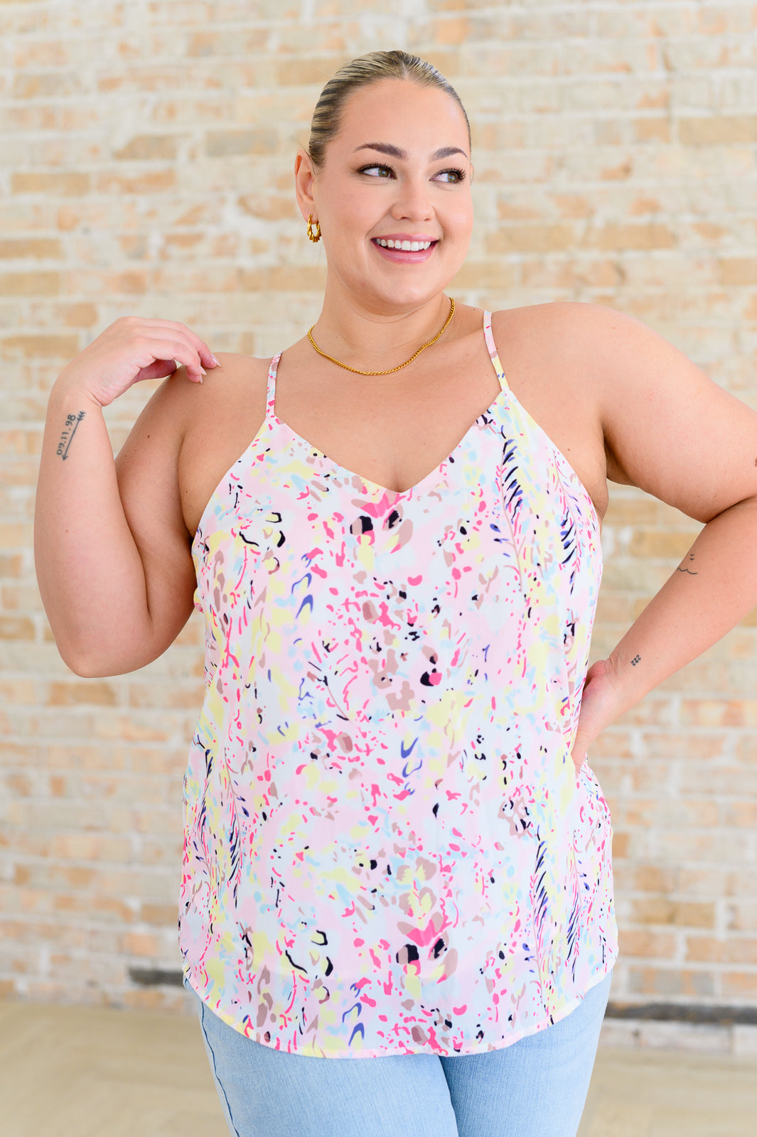 A woman wearing a multicolored floral printed cami with a v-neckline and adjustable spaghetti straps.
