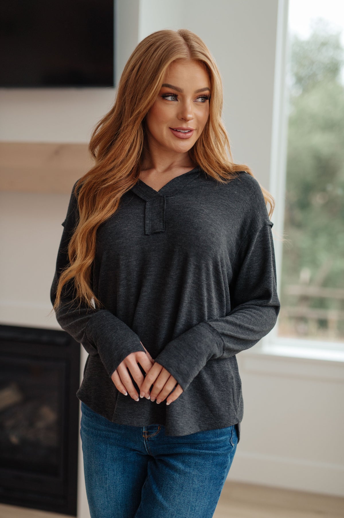 A woman wearing a charcoal gray long sleeve top with a V-neckline and thumb holes, standing indoors.