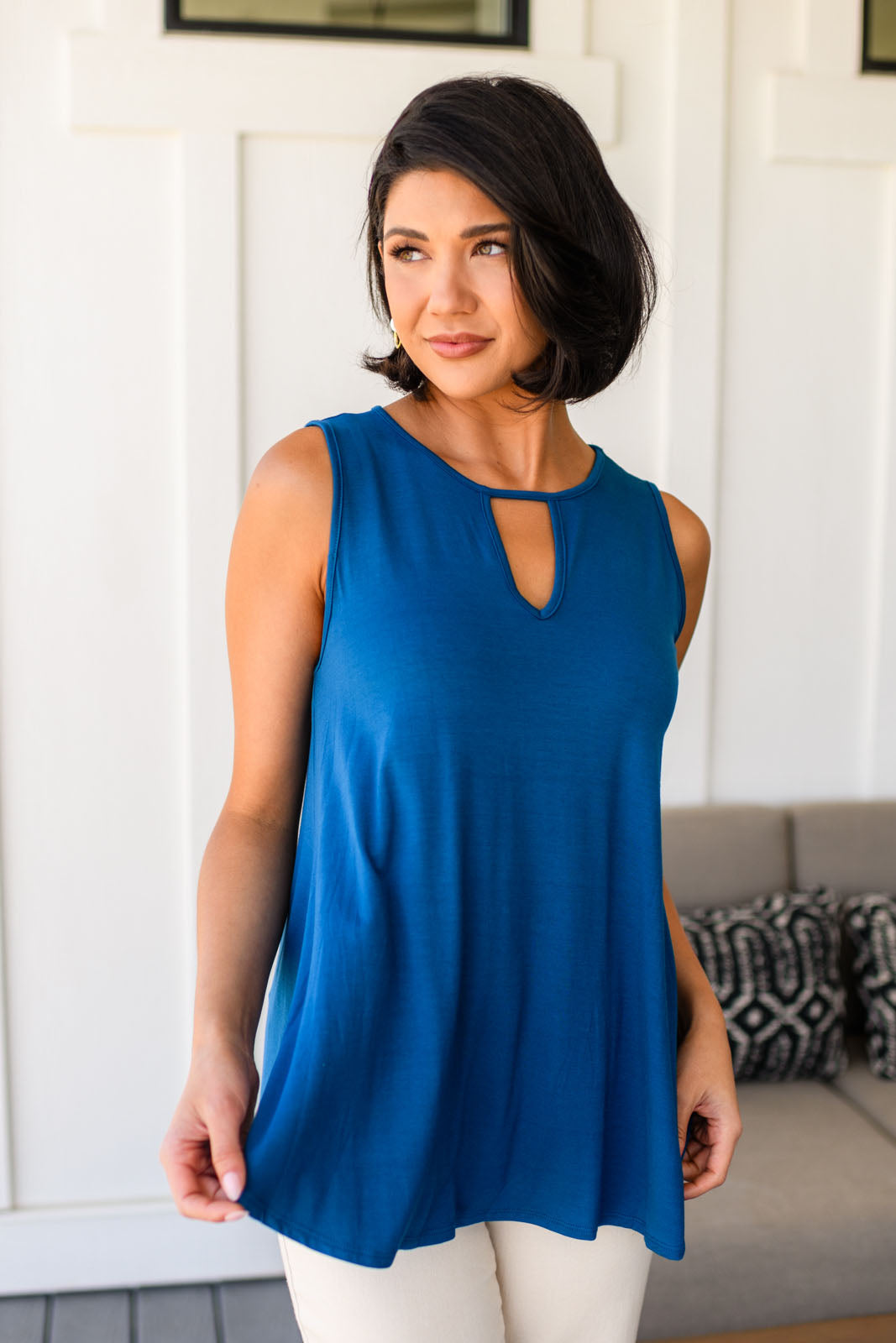 Woman wearing a blue sleeveless tank top with a cutout design, standing in a room with a white wall and gray couch