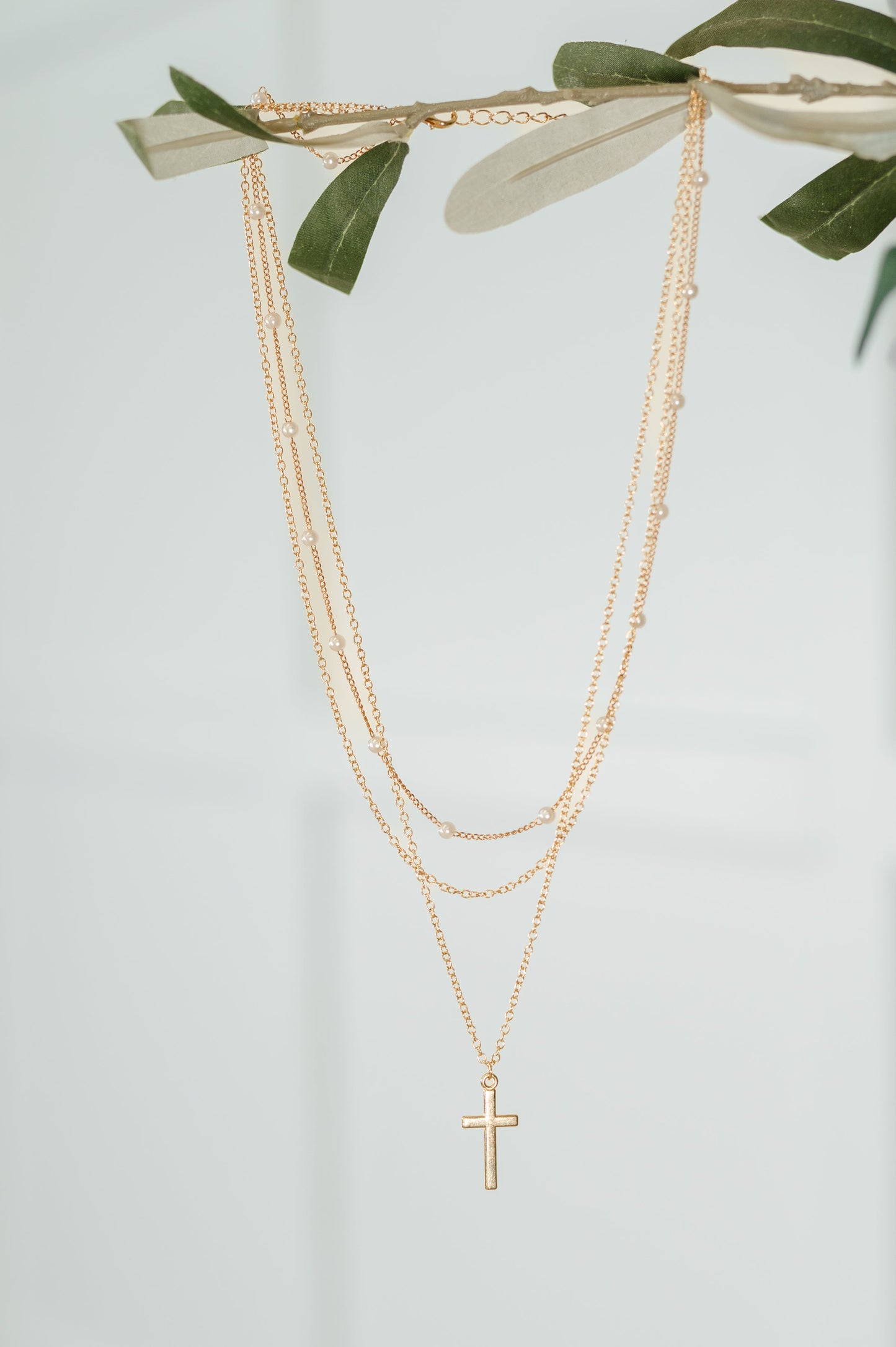 Gold necklace with a cross pendant on a light gray background