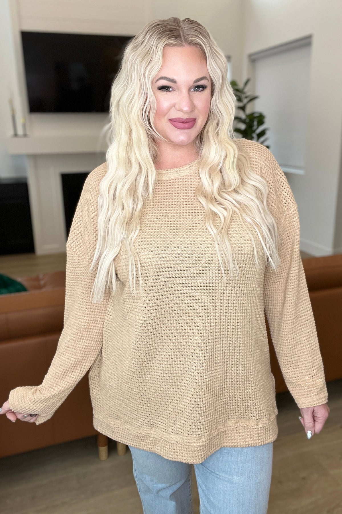 Woman wearing a beige waffle knit pullover with a drop shoulder and side slits.